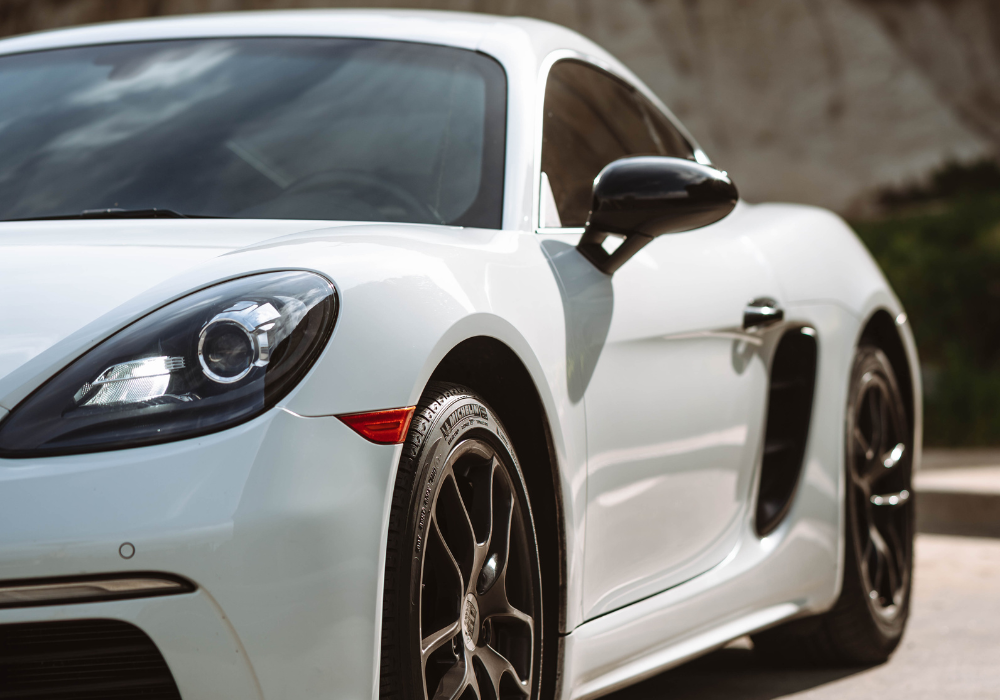 Close-up of a white sports car with black side mirror and black wheels, parked outdoors.