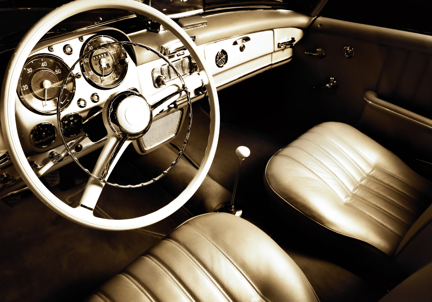 Interior view of a vintage car showing a steering wheel, dashboard with gauges, and leather seats in sepia tone.