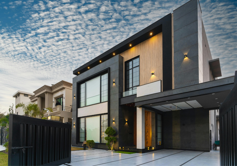 Modern two-story house with large windows, exterior lighting, and a driveway, evening sky with scattered clouds.