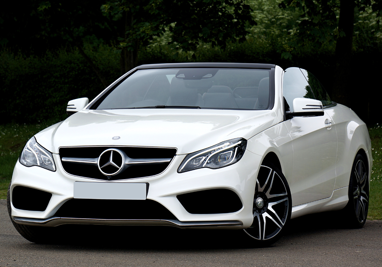 White Mercedes-Benz convertible car parked outdoors on a paved surface with trees in the background.