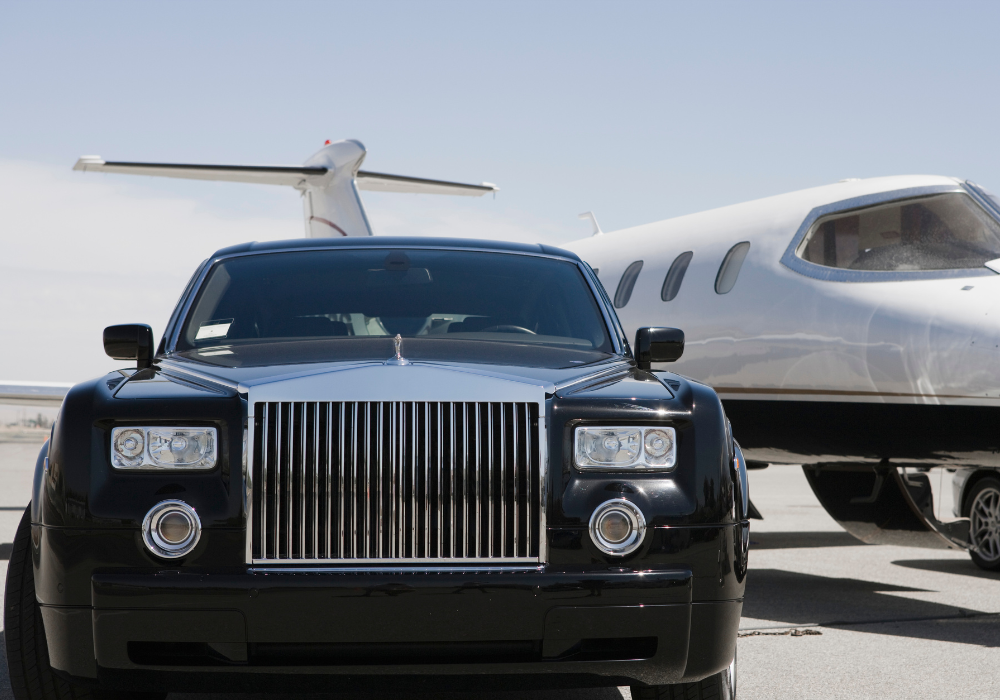 A black luxury car and a private jet airplane parked on a tarmac.