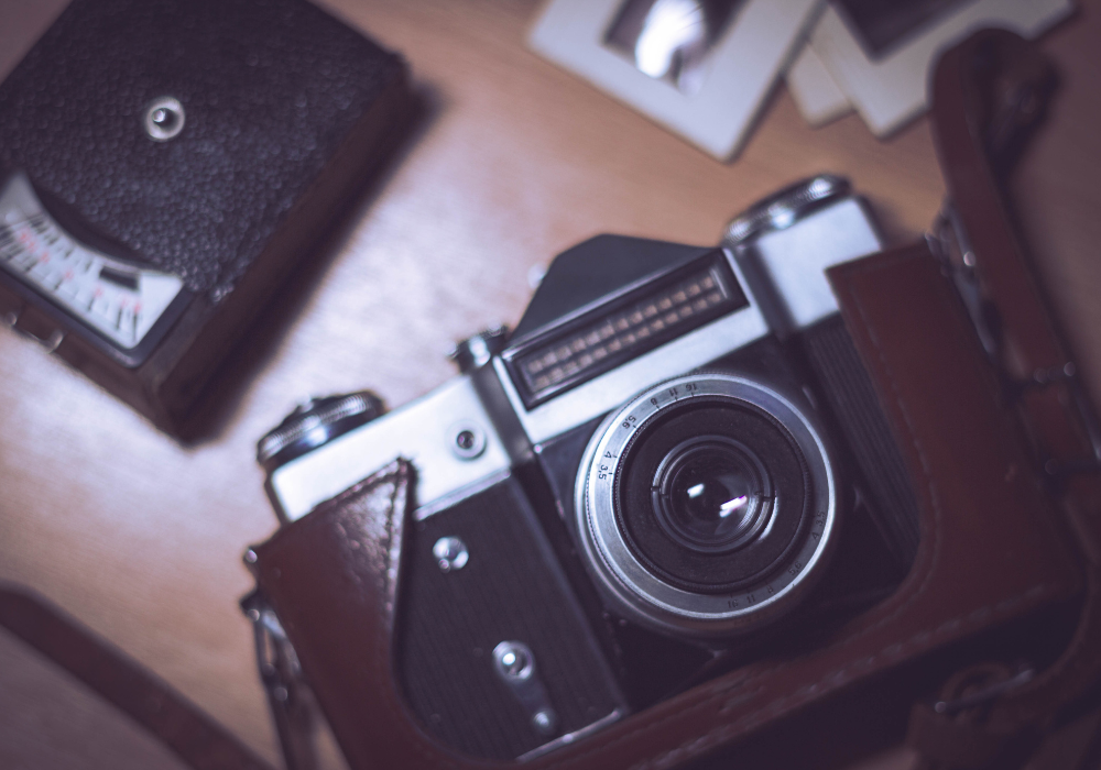 A vintage camera with a leather case on a wooden surface, with an undeveloped film roll and photographs nearby.