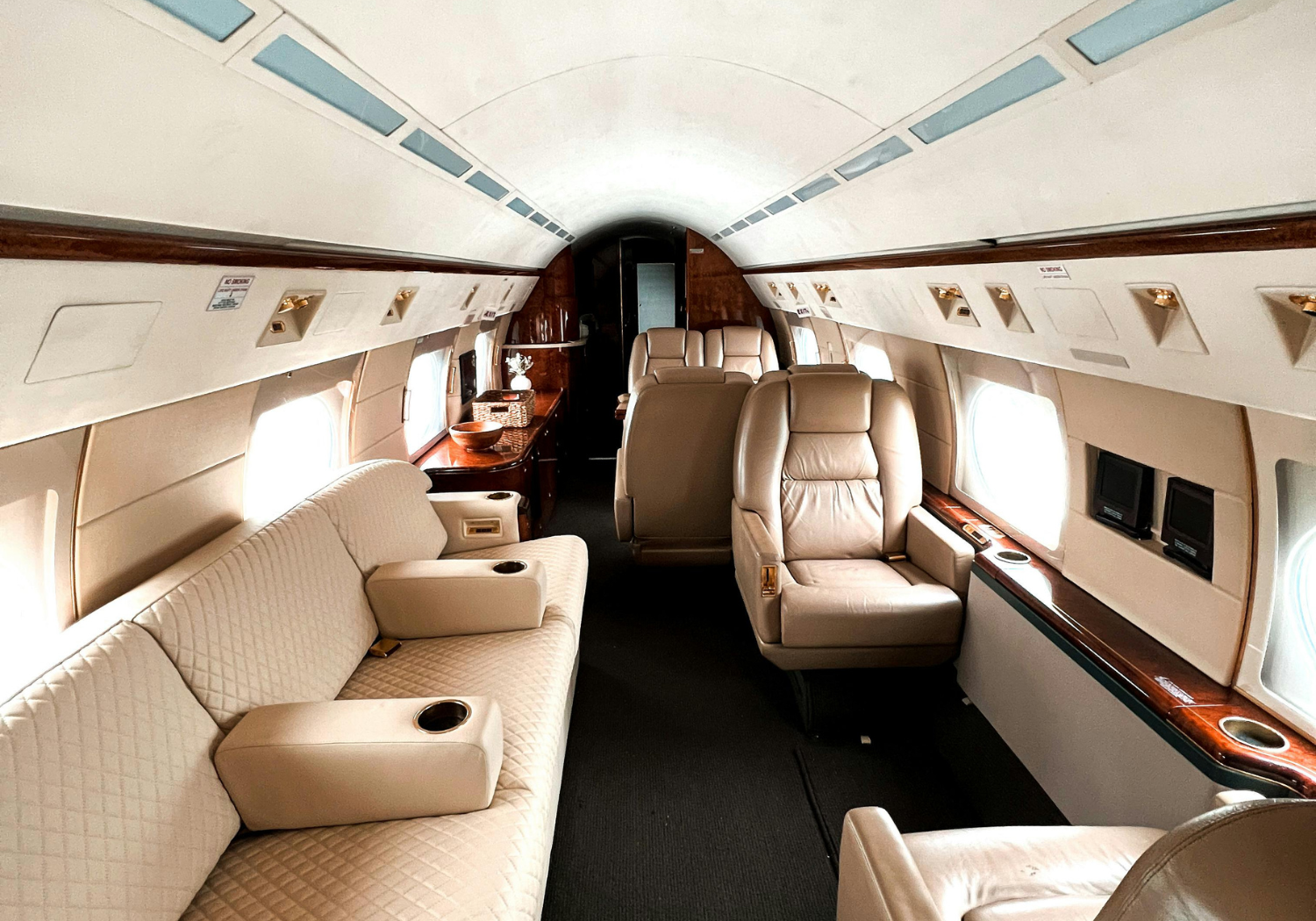 Interior of a private jet with beige leather seats, windows, and wood accents.