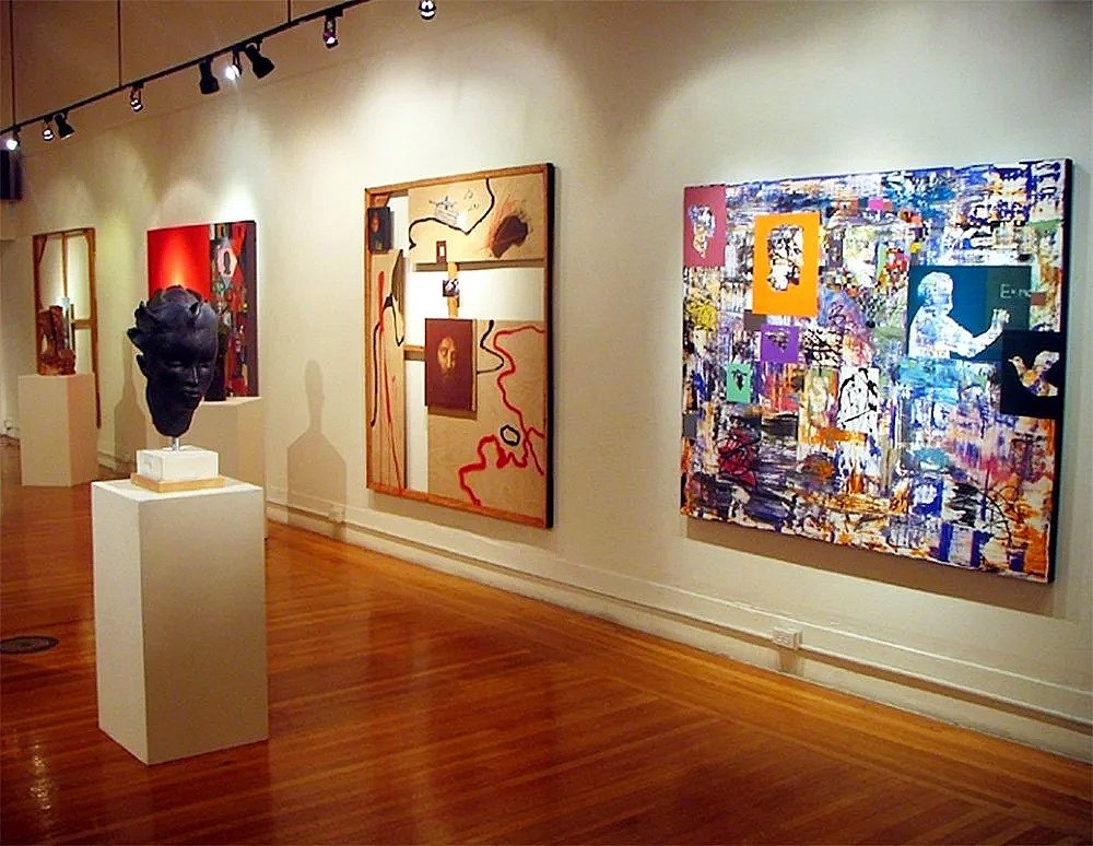 A gallery scene with a sculpture of a head in the foreground and several of Rodney's paintings in the background.
