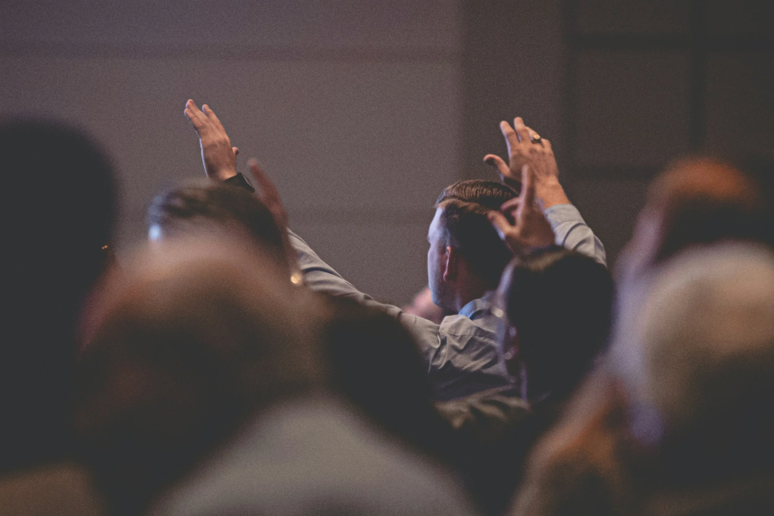 People in a conference room raising their hands during a presentation or discussion, viewed from behind.