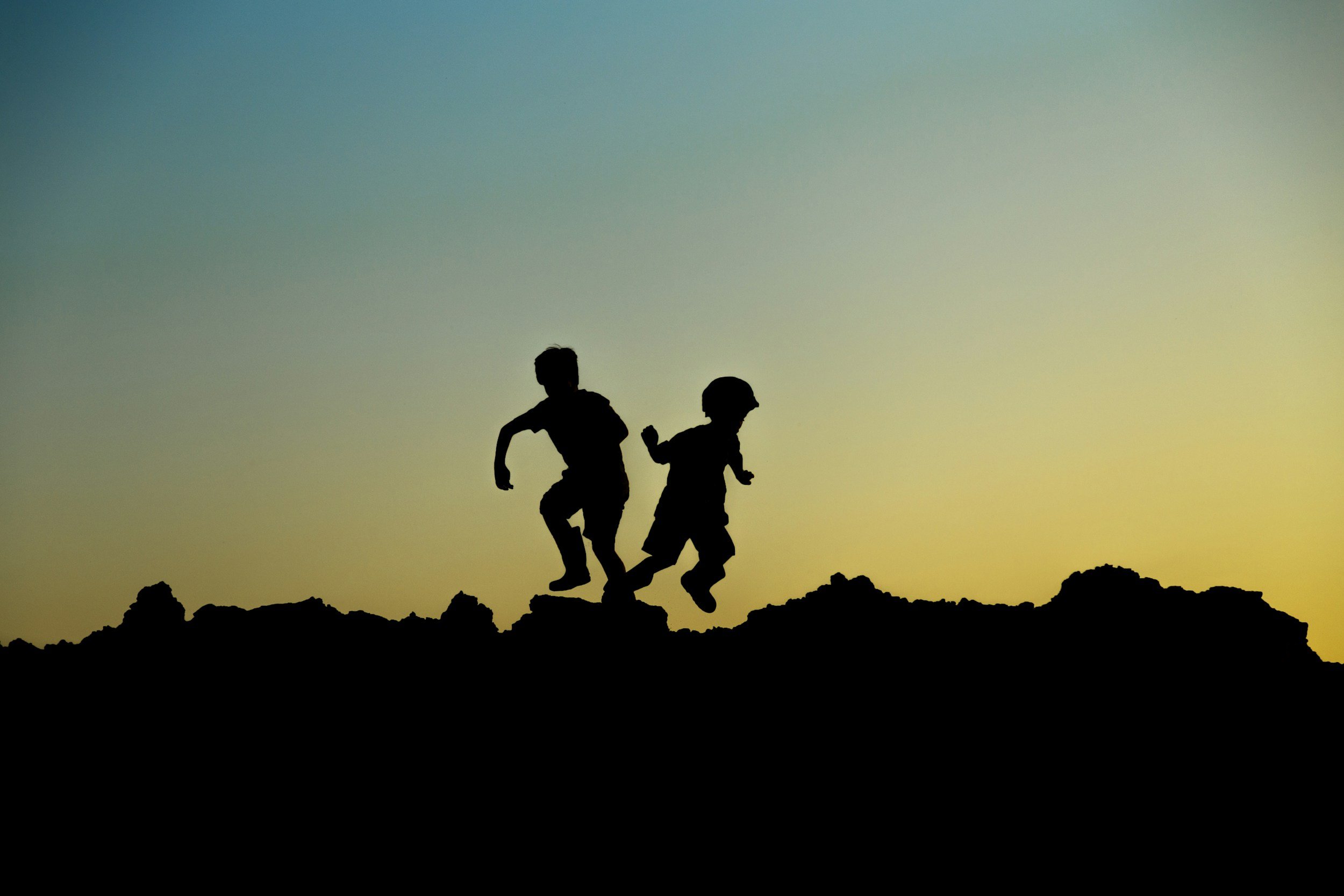 Silhouette of two children running on rocky terrain during sunset.
