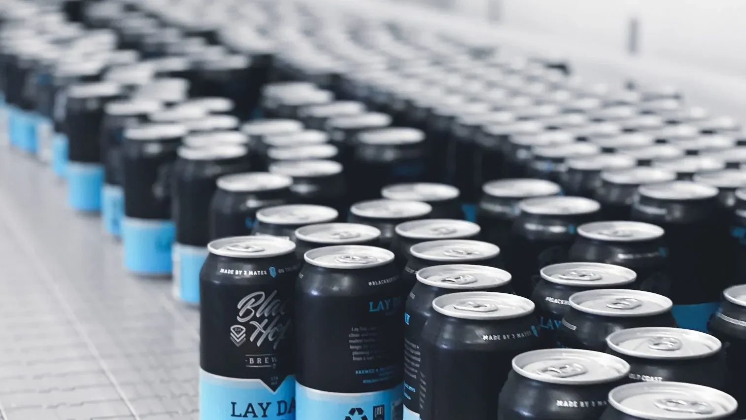 Row of black and blue cans of beer on a metal shelf in a warehouse.