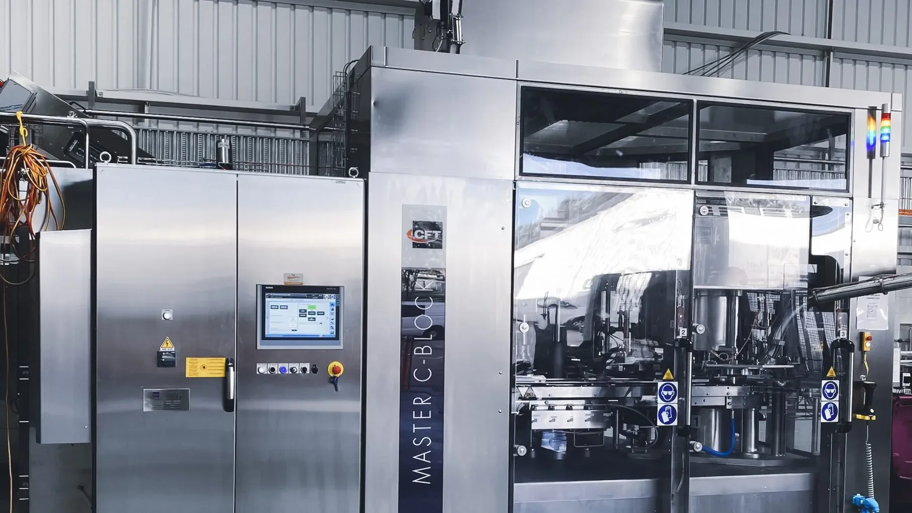 Industrial machine in a factory with a touchscreen control panel and safety warning signs.