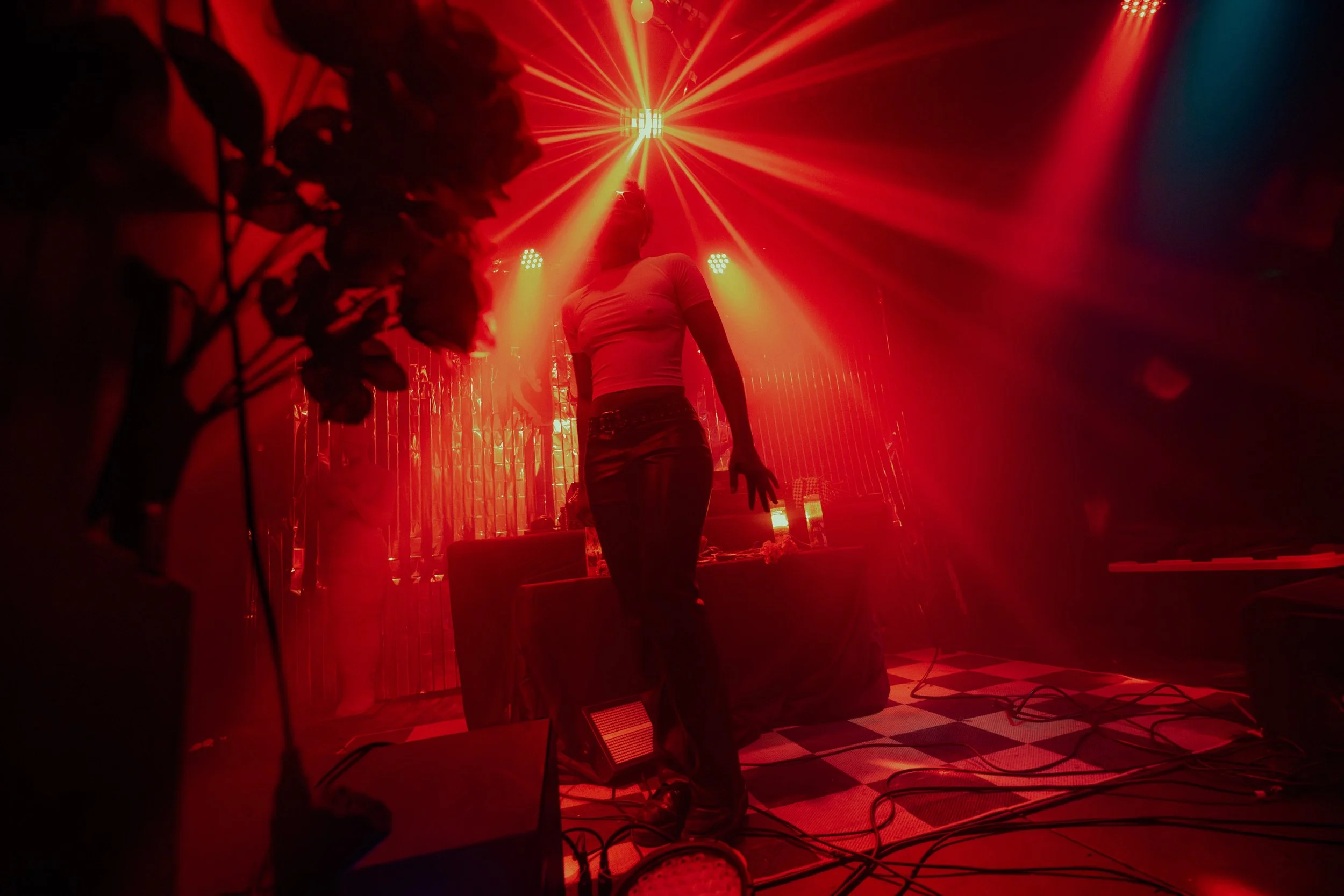 Person on stage under red and yellow laser lights, with floral decorations on the side and a checkered floor. L'objectif Photography: New Orleans Wedding, Event, and Portrait Photographer