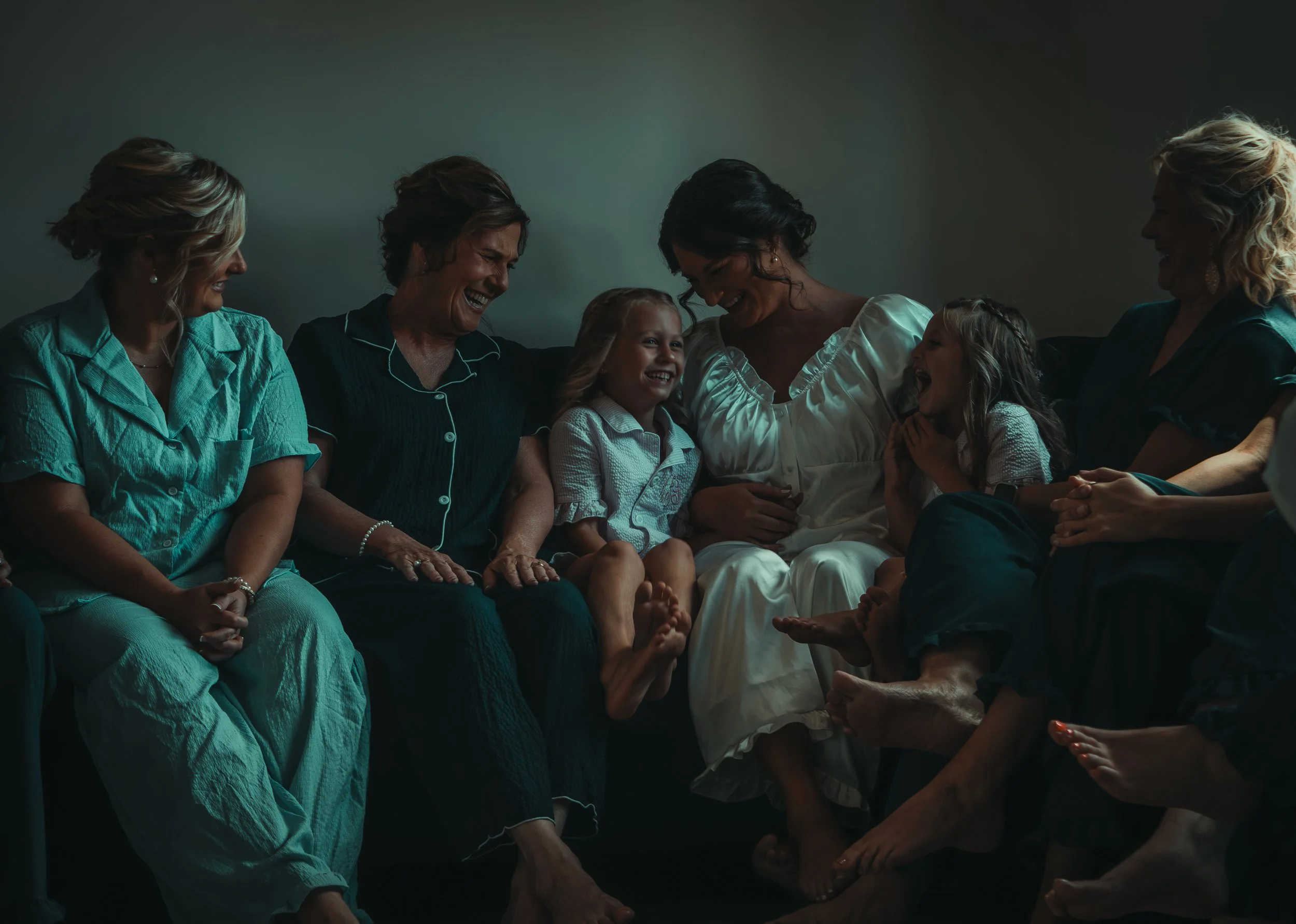 Group of women and two young girls sitting together on a couch, smiling and enjoying each other's company.