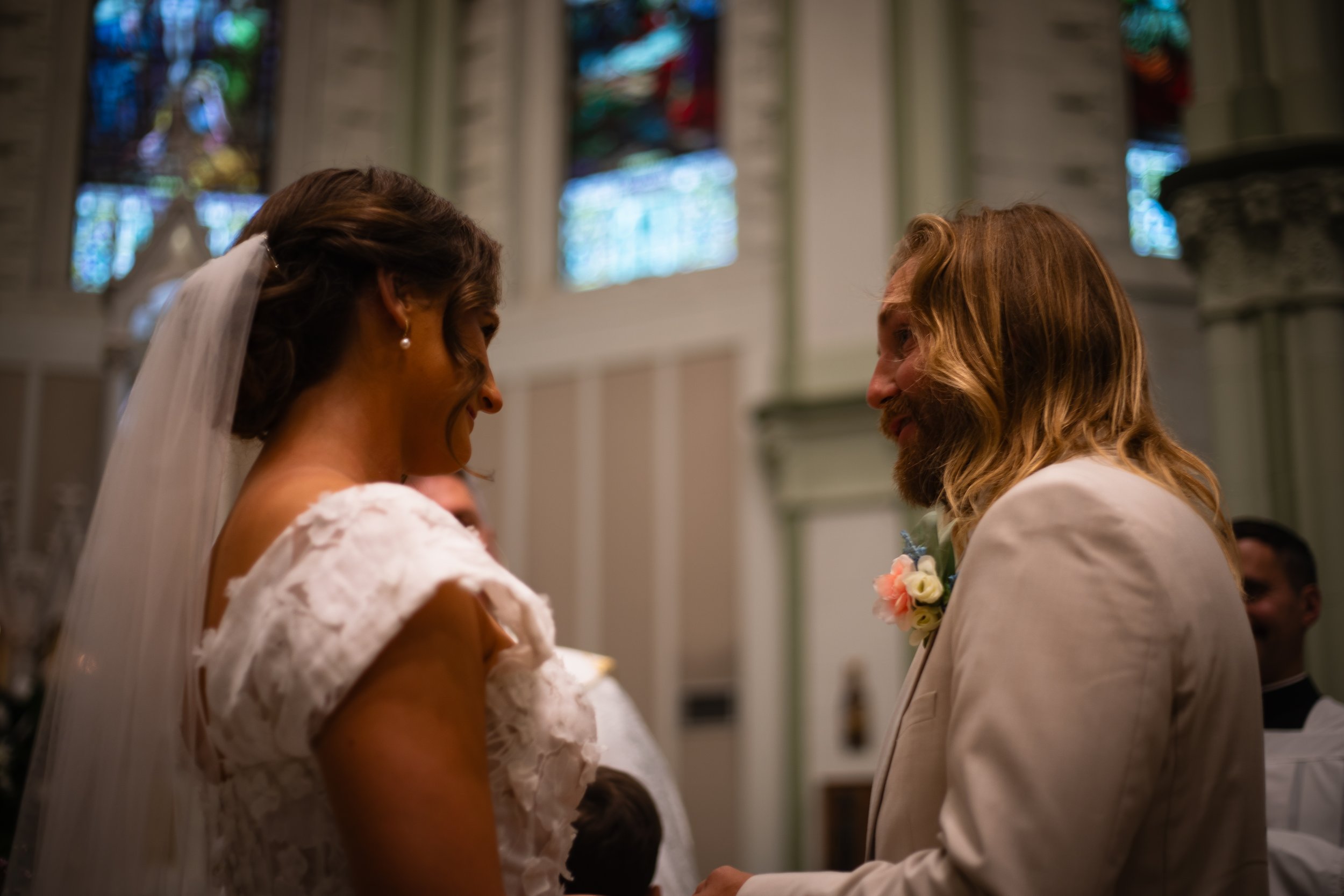 A bride and groom facing each other during their wedding ceremony inside a church, with stained glass windows in the background. L'objectif Photography: New Orleans Wedding, Event, and Portrait Photographer