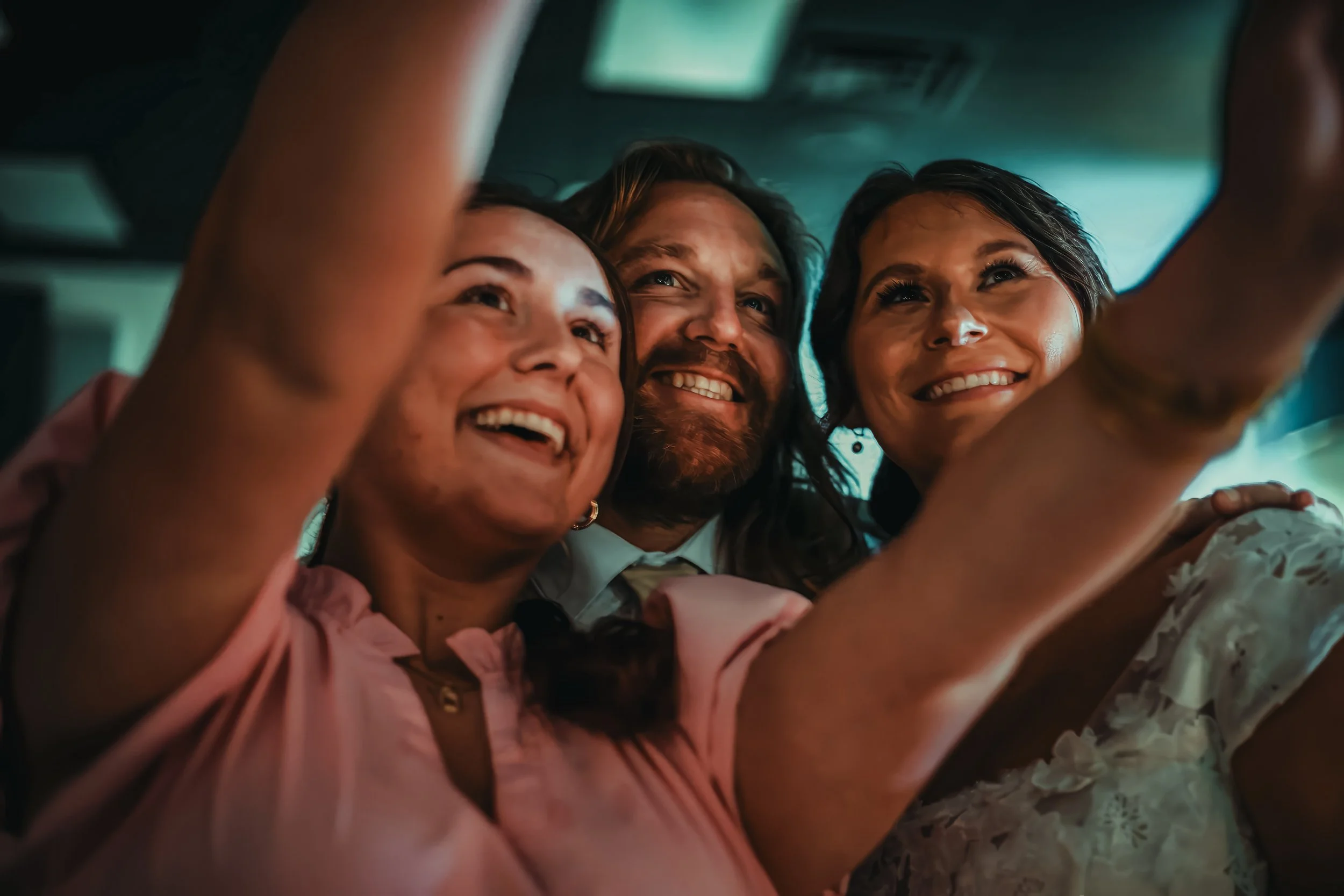 Three people smiling and taking a selfie together inside a vehicle.