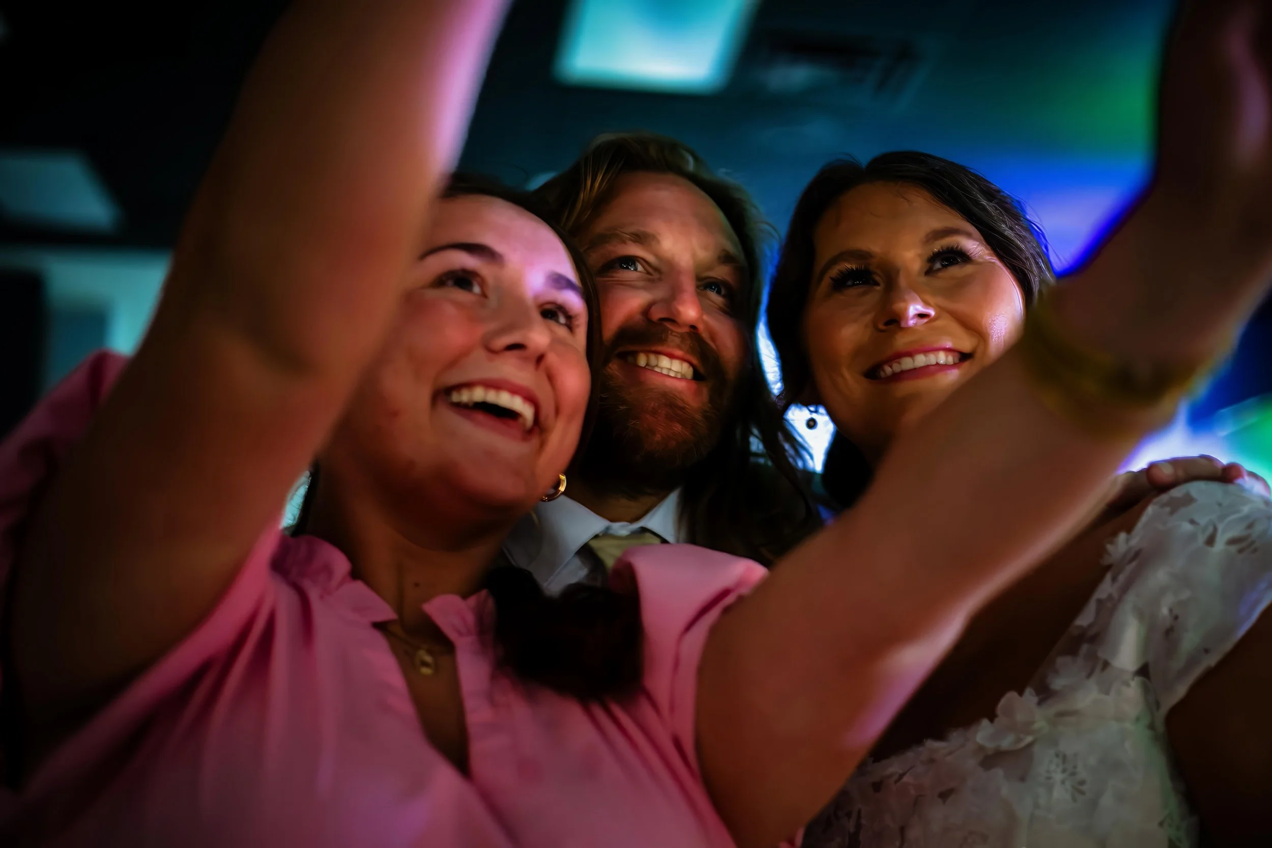 Three smiling people taking a selfie in a dimly lit room with colorful lights. L'objectif Photography: New Orleans Wedding, Event, and Portrait Photographer