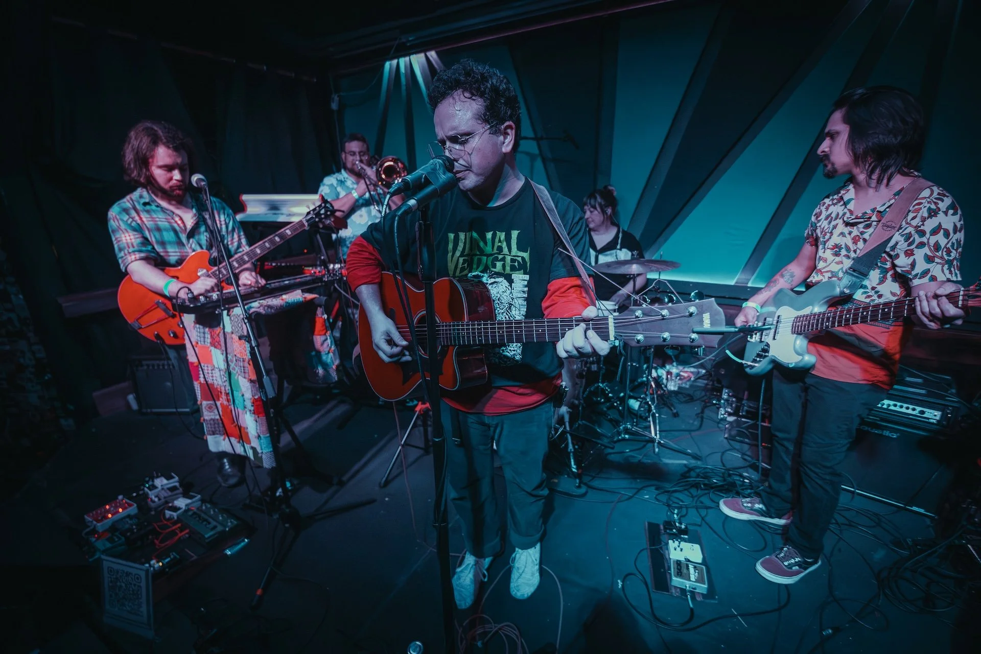 A band performing on stage with multiple musicians playing guitars, trumpet, and drums, illuminated by stage lights. L'objectif Photography: New Orleans Wedding, Event, and Portrait Photographer