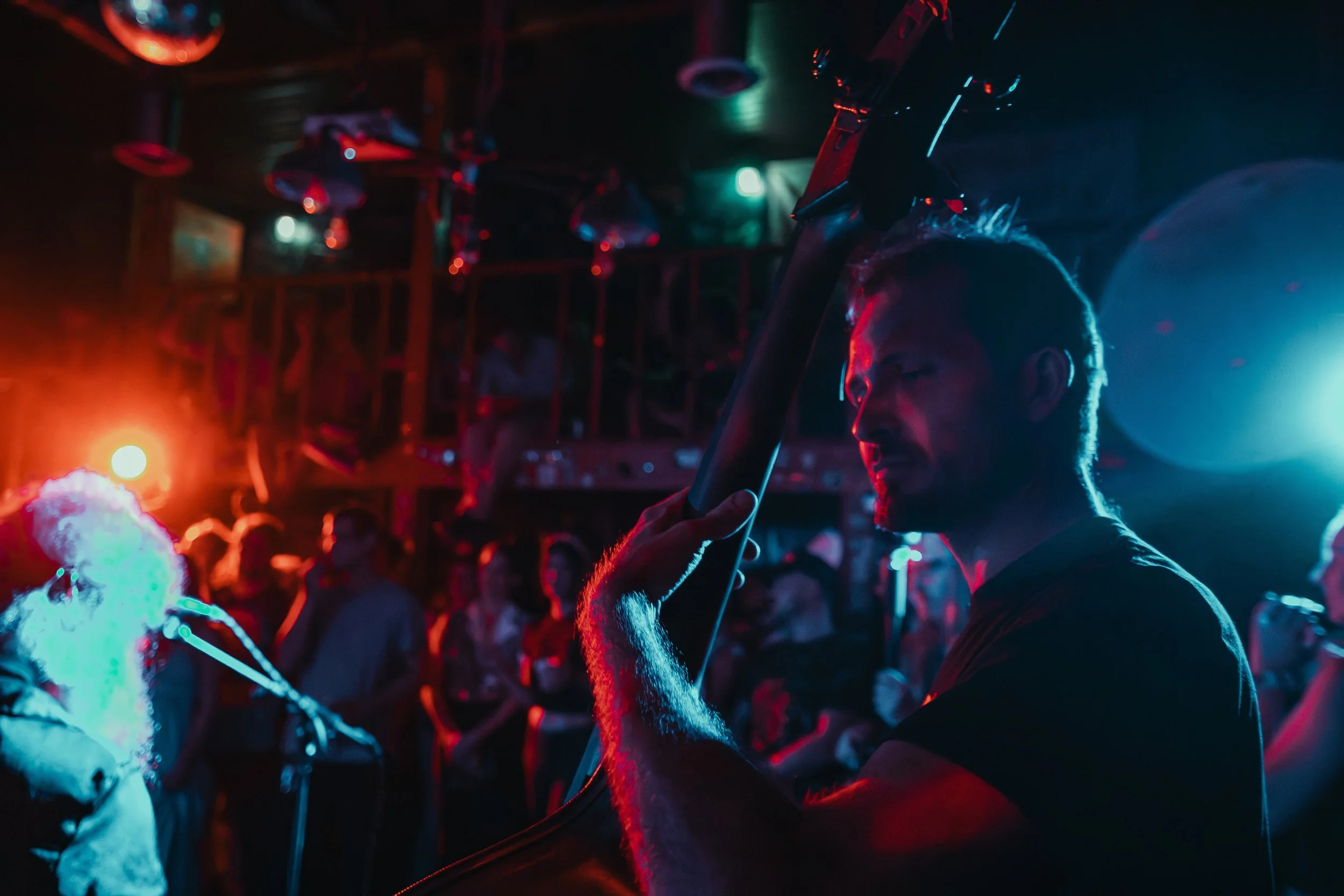 A person with glasses holding a sword or glow stick at a lively party or concert with neon and colorful lighting, surrounded by other attendees. L'objectif Photography: New Orleans Wedding, Event, and Portrait Photographer