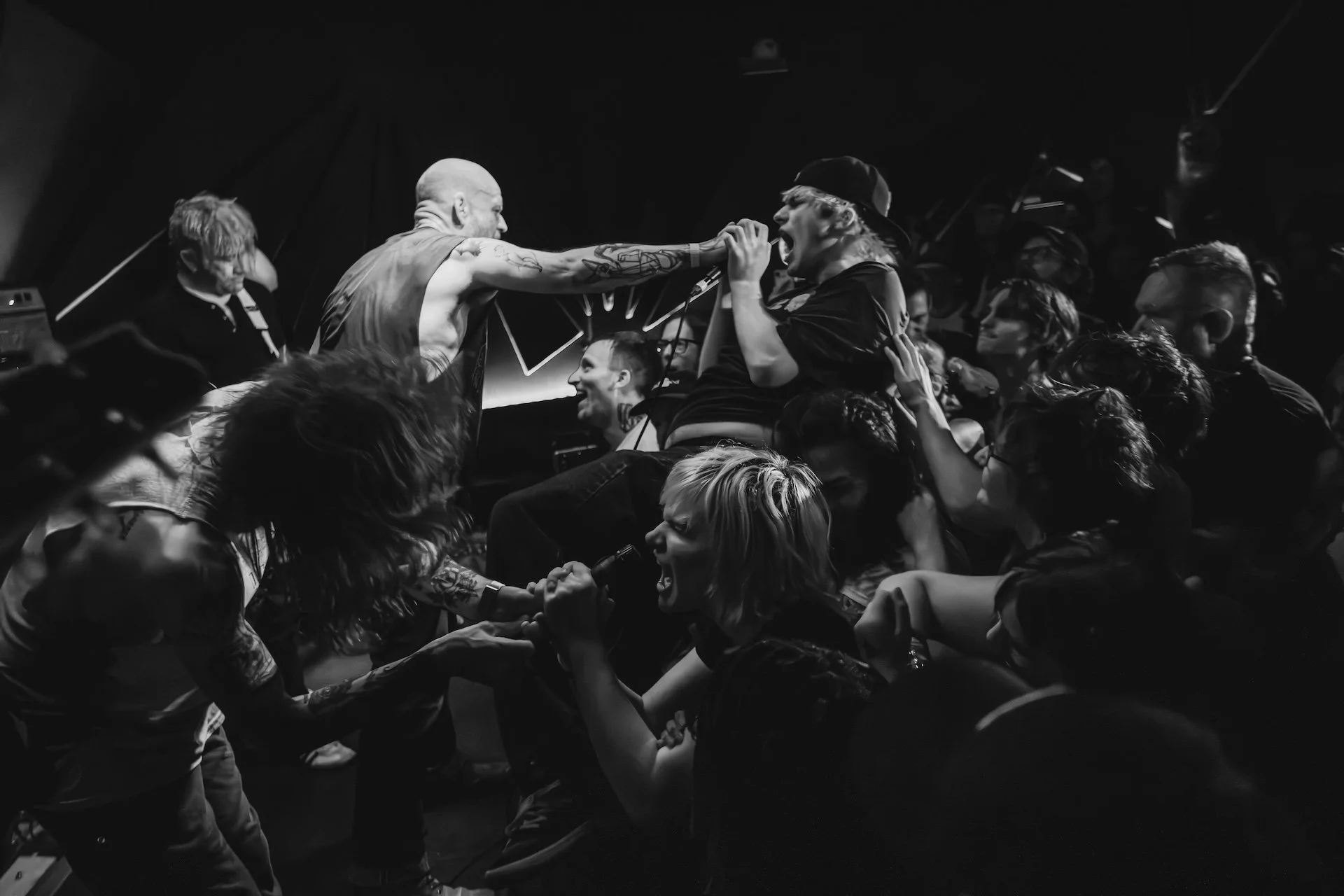 Black and white photo of a concert scene with a singer passionately performing on stage, surrounded by fans reaching and grabbing him, some with arms outstretched, with a dark background. L'objectif Photography: New Orleans Wedding, Event, and Portra