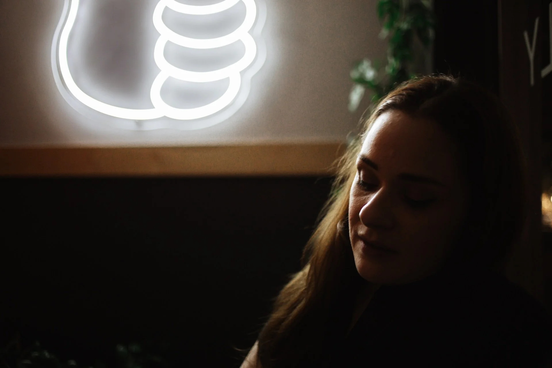 A woman with long brown hair is sitting in a dimly lit room with her eyes closed, illuminated by a white neon light shaped like a cactus in the background. L'objectif Photography: New Orleans Wedding, Event, and Portrait Photographer
