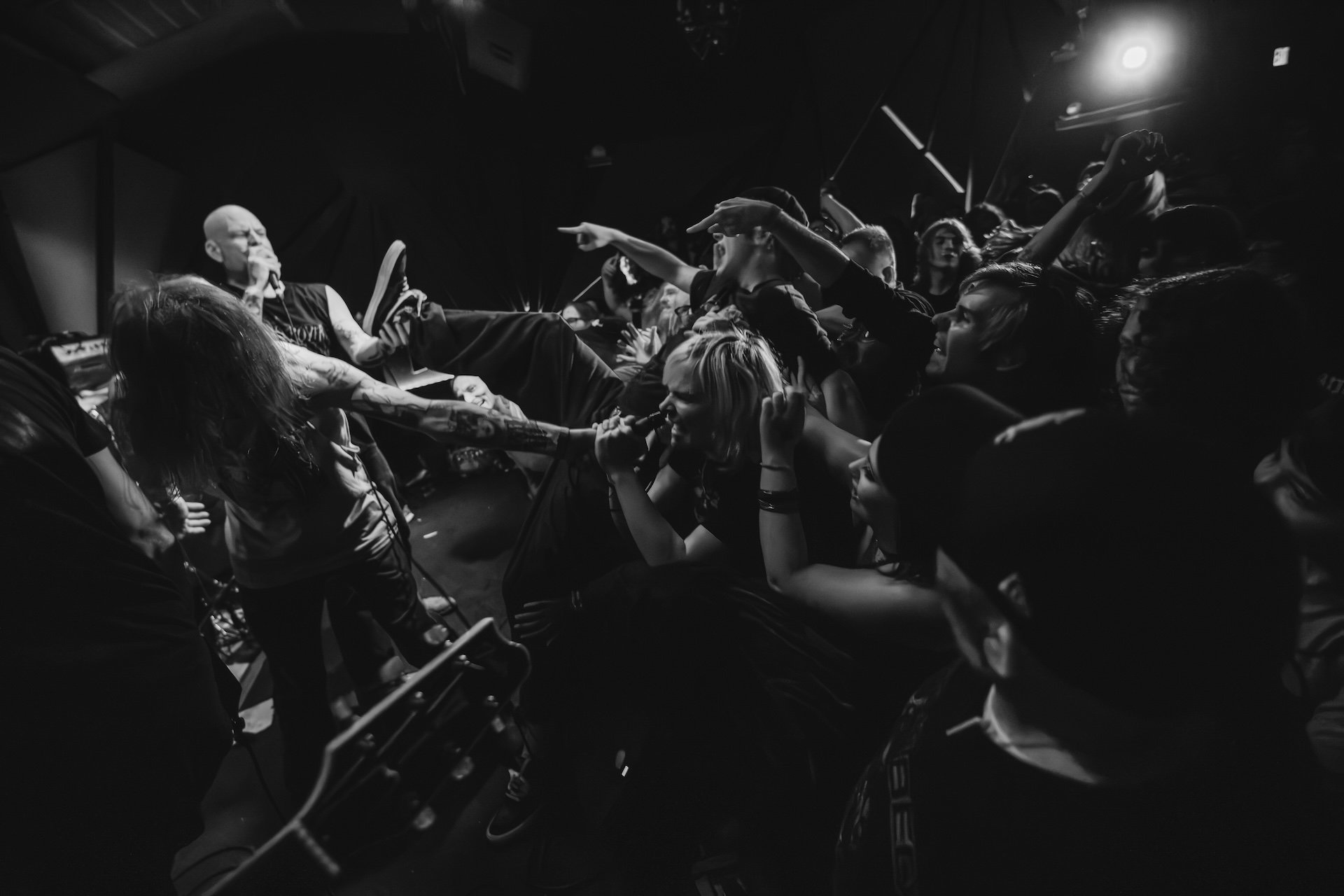 Black and white photo of a live music concert with a singer performing on stage, reaching out towards the audience, while the crowd passionately reaches back. The audience is close to the stage, some with arms extended, and the scene is energetically