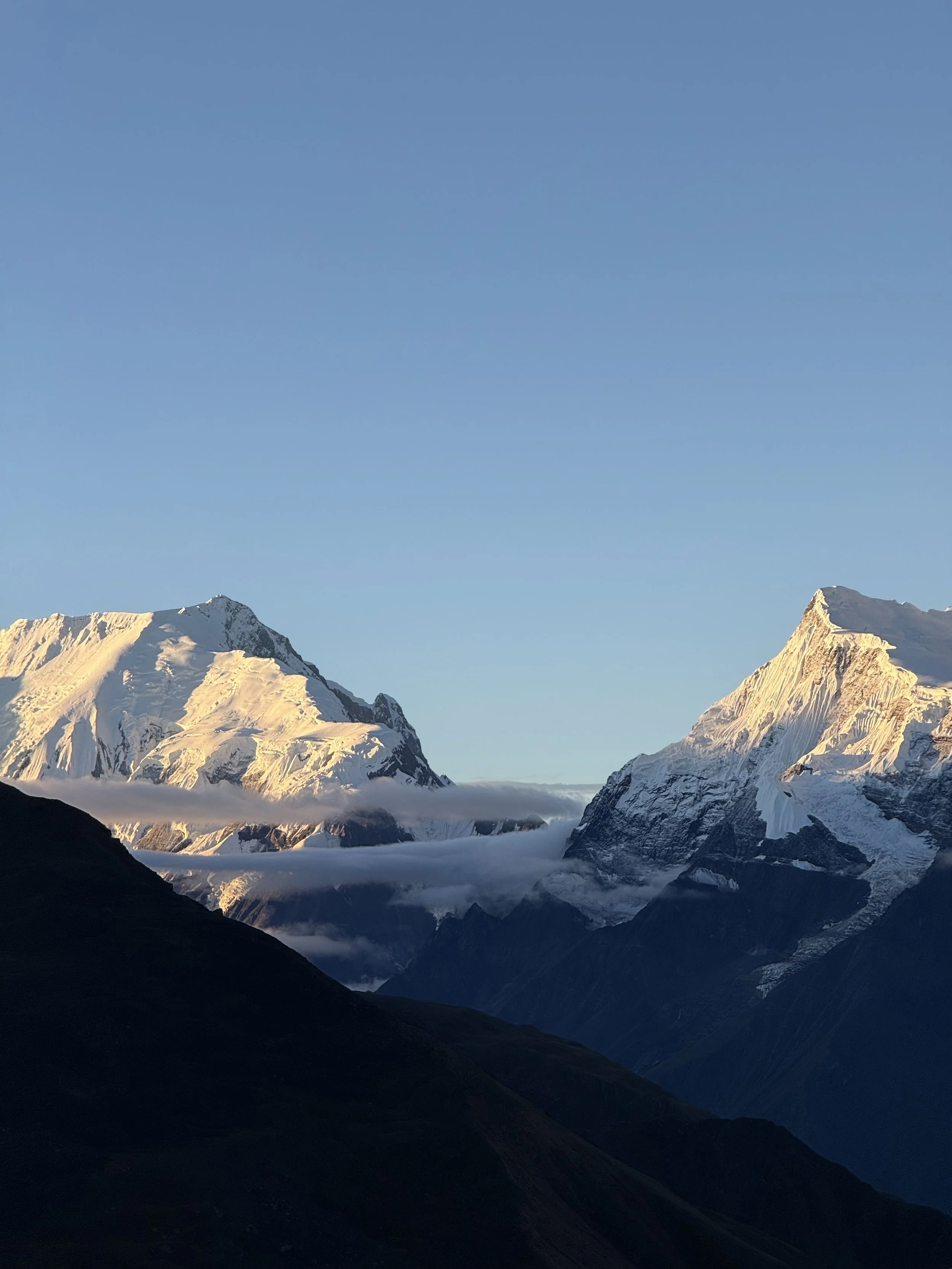 Snow-capped mountain peaks under a clear blue sky with dark green hills in the foreground.