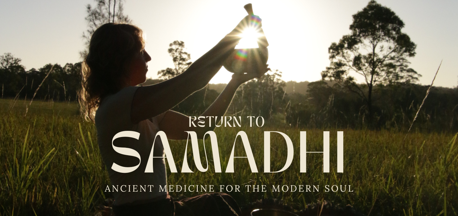 A woman practicing yoga outdoors in a grassy field with trees in the background during sunset, holding her hands in a prayer position with sunlight shining through her hands.