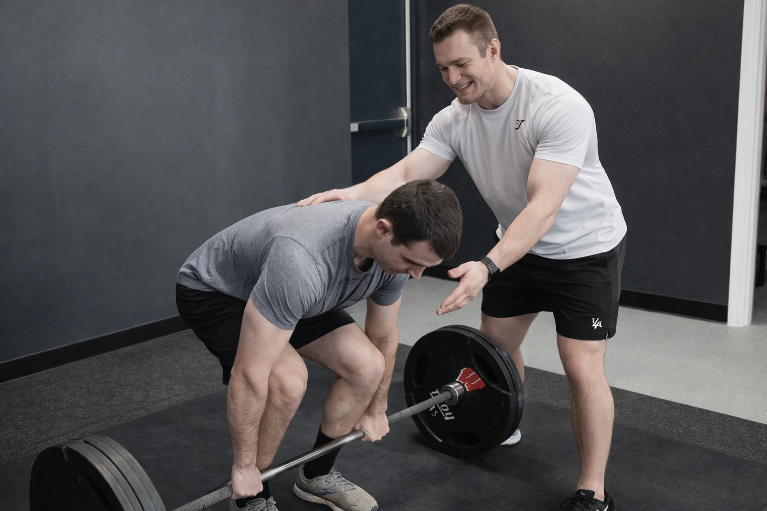 Personal trainer coaching a man doing a deadlift with a barbell in a gym.