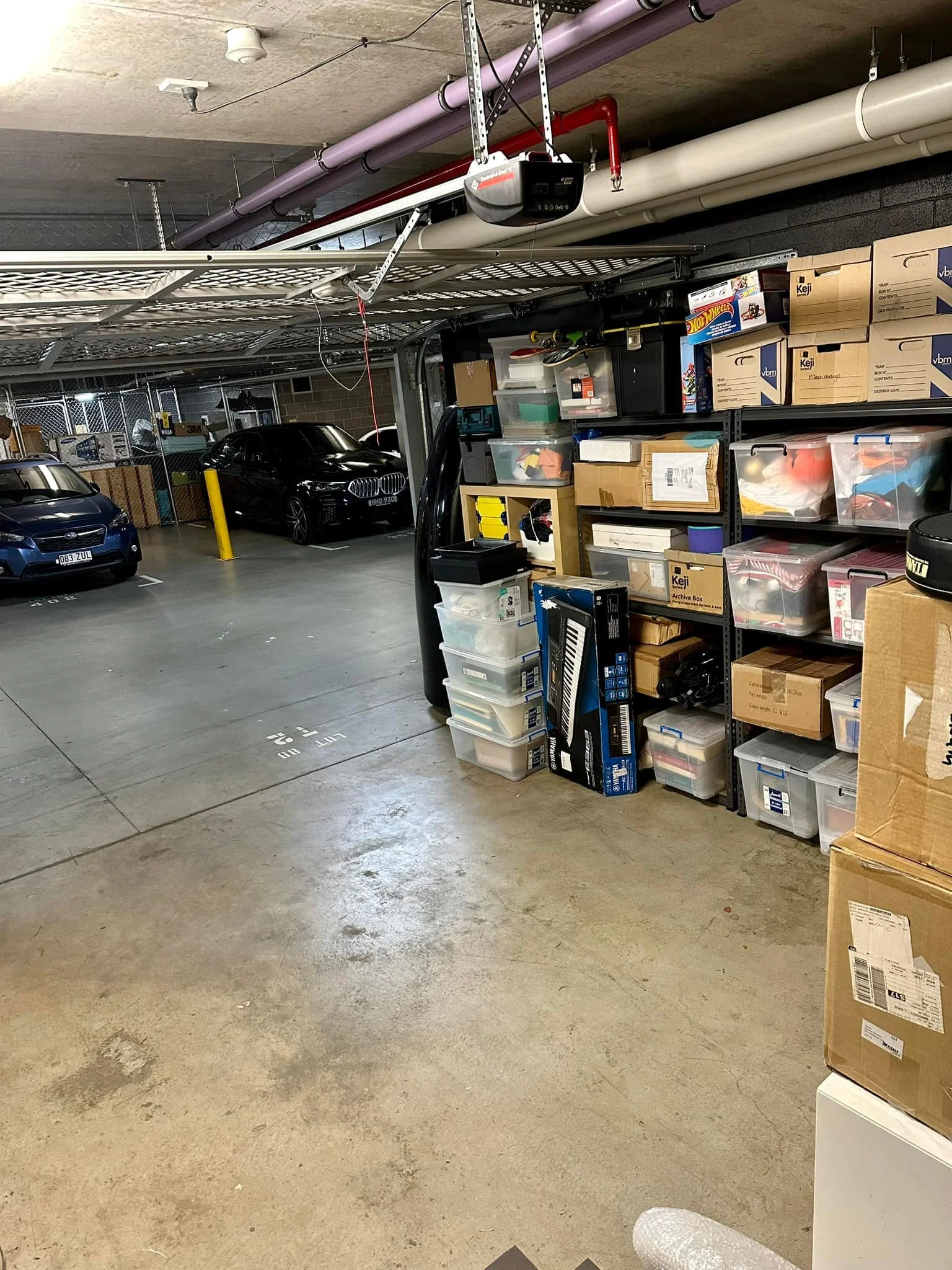 Indoor parking garage with parked cars and shelves filled with storage bins and boxes.