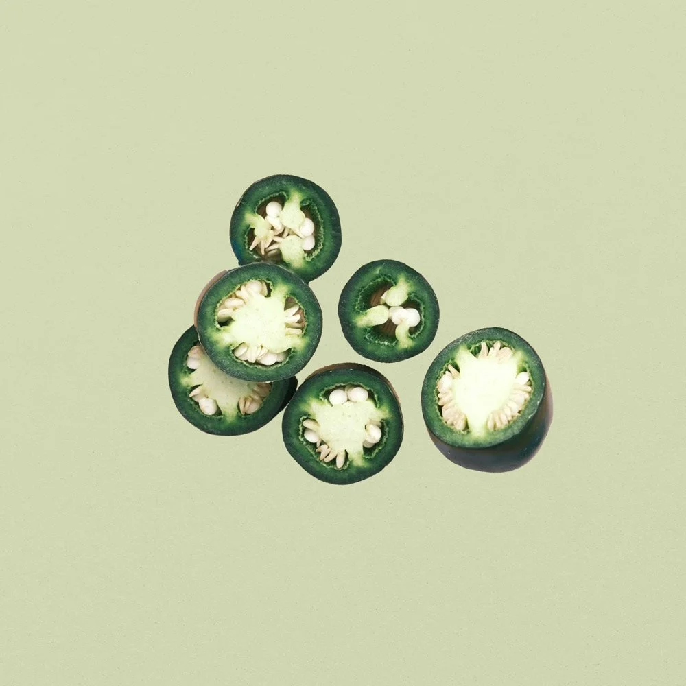 Sliced jalapeño peppers on a light green background.