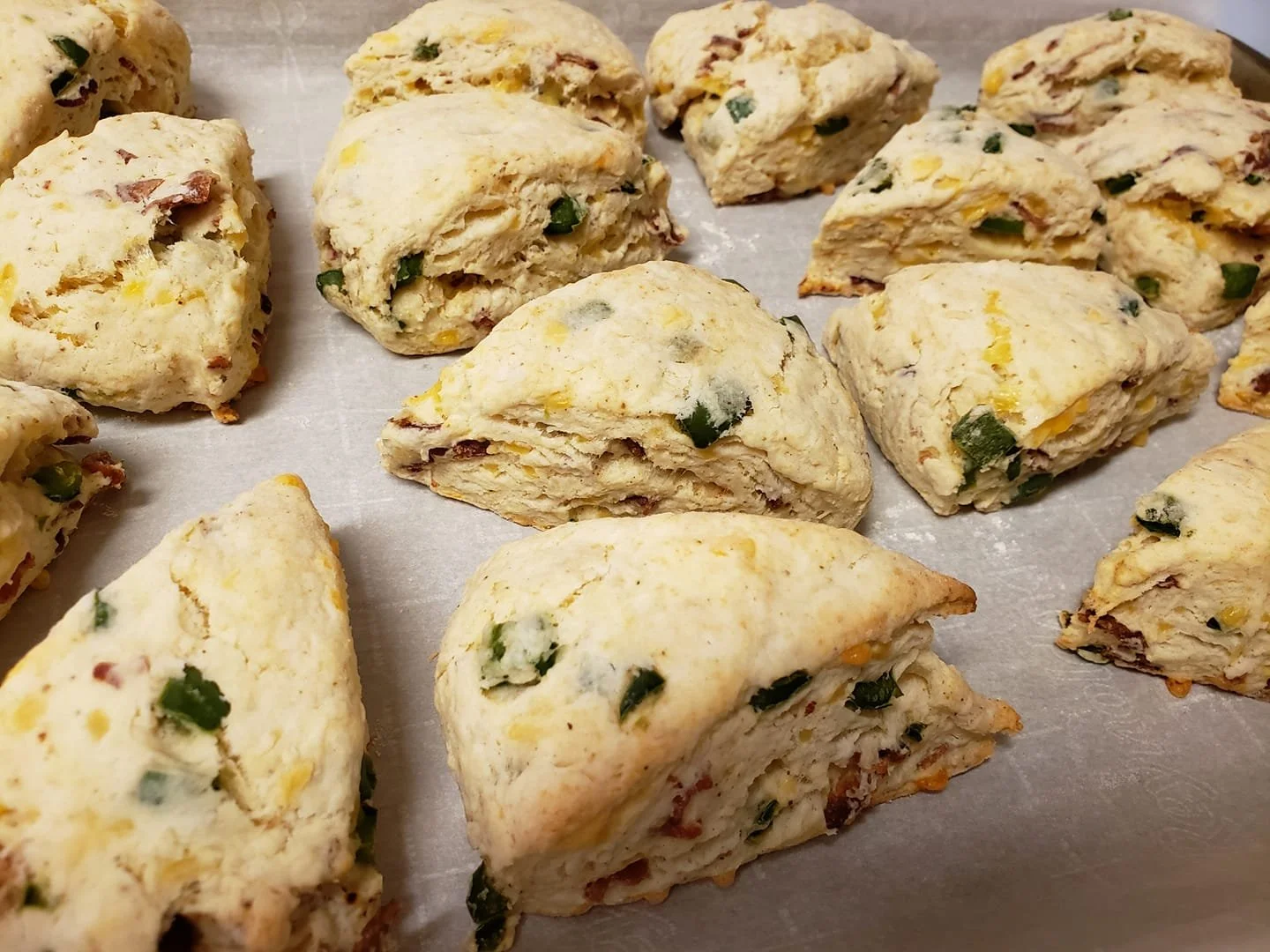 Unbaked scones with bits of green onions, cheese, and possibly bacon, on a baking sheet lined with parchment paper.