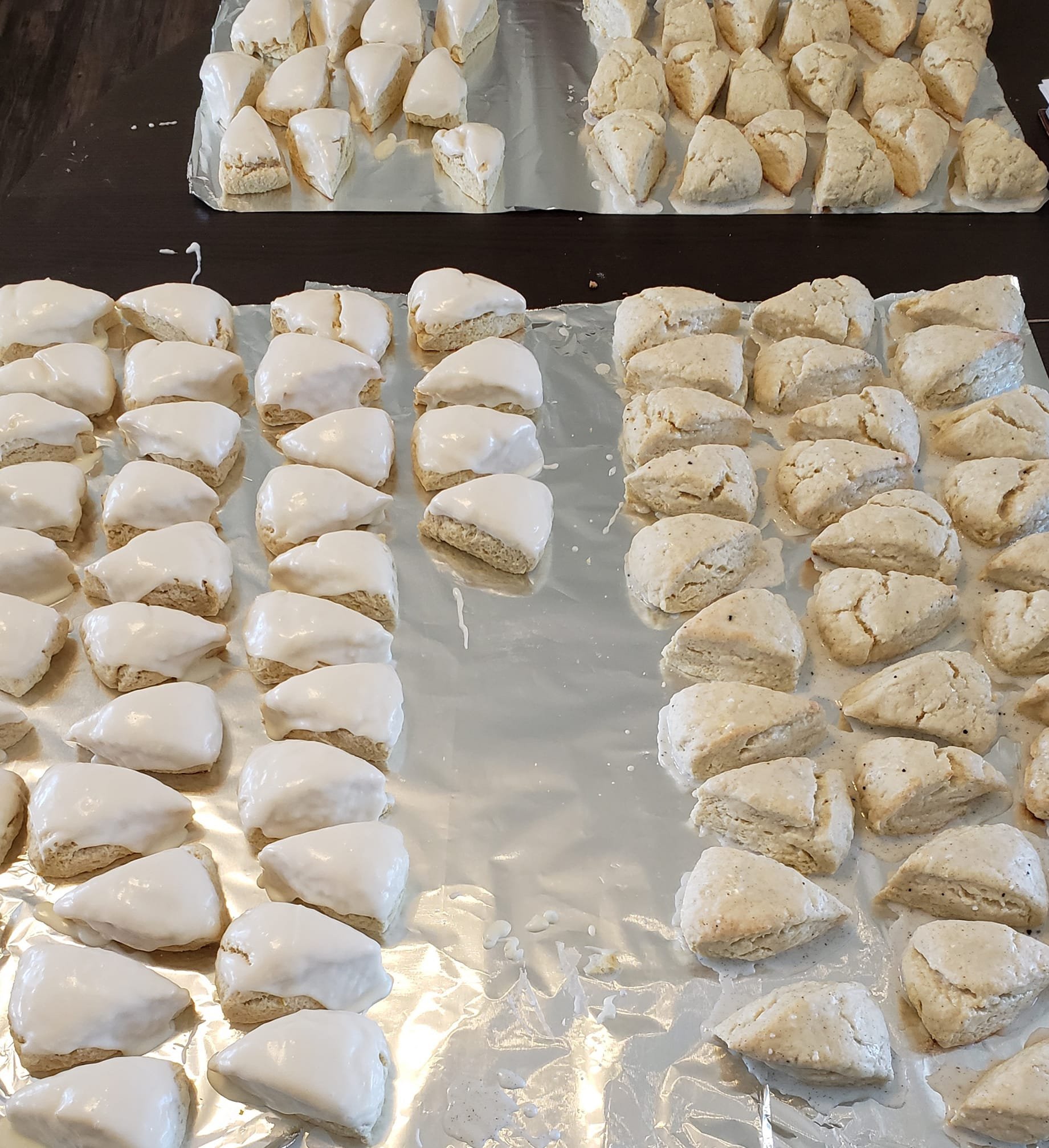 Rows of unbaked scones on baking sheets, some topped with white icing.