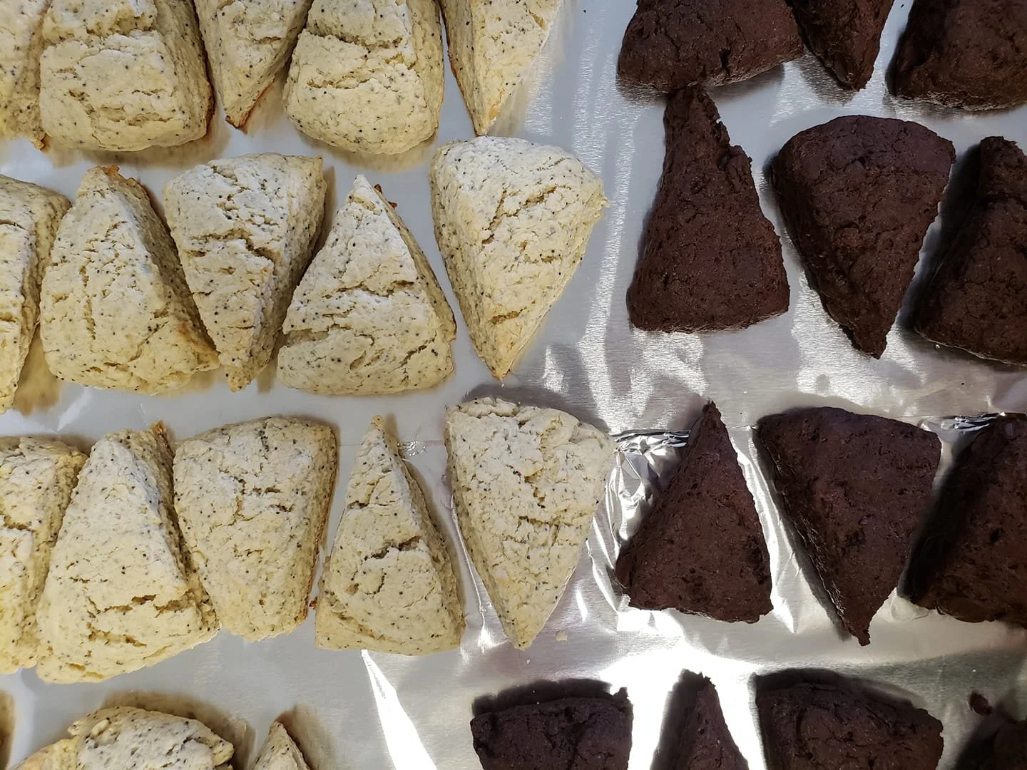 An assortment of scones and cookies on a silver tray, with light-colored scones on the left and dark chocolate cookies on the right.