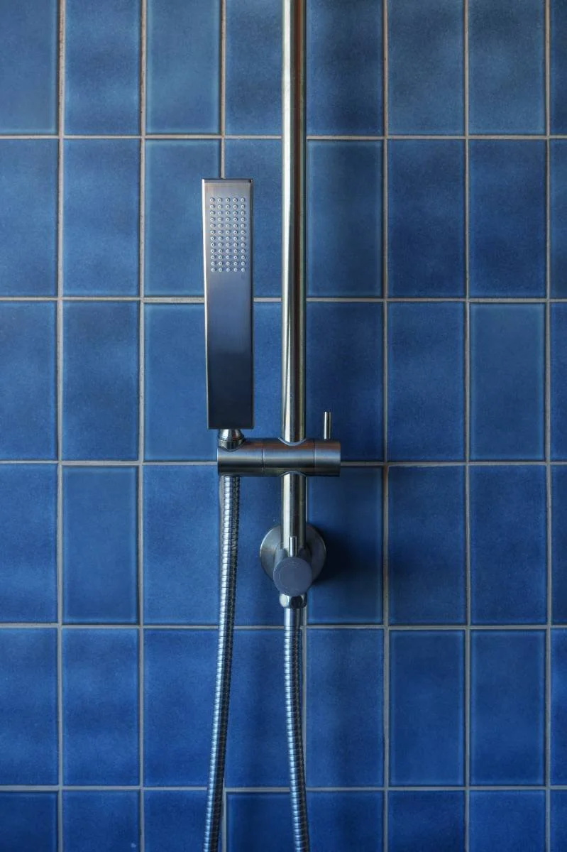 A balcony patio setting with a white modern chair, a wooden side table with a cheese platter, grapes, and dip, a glass of white wine, and a bottle of wine labeled 'Bay of Shoals Kangaroo Island,' with a black metal wall and a partly cloudy sky in the background.