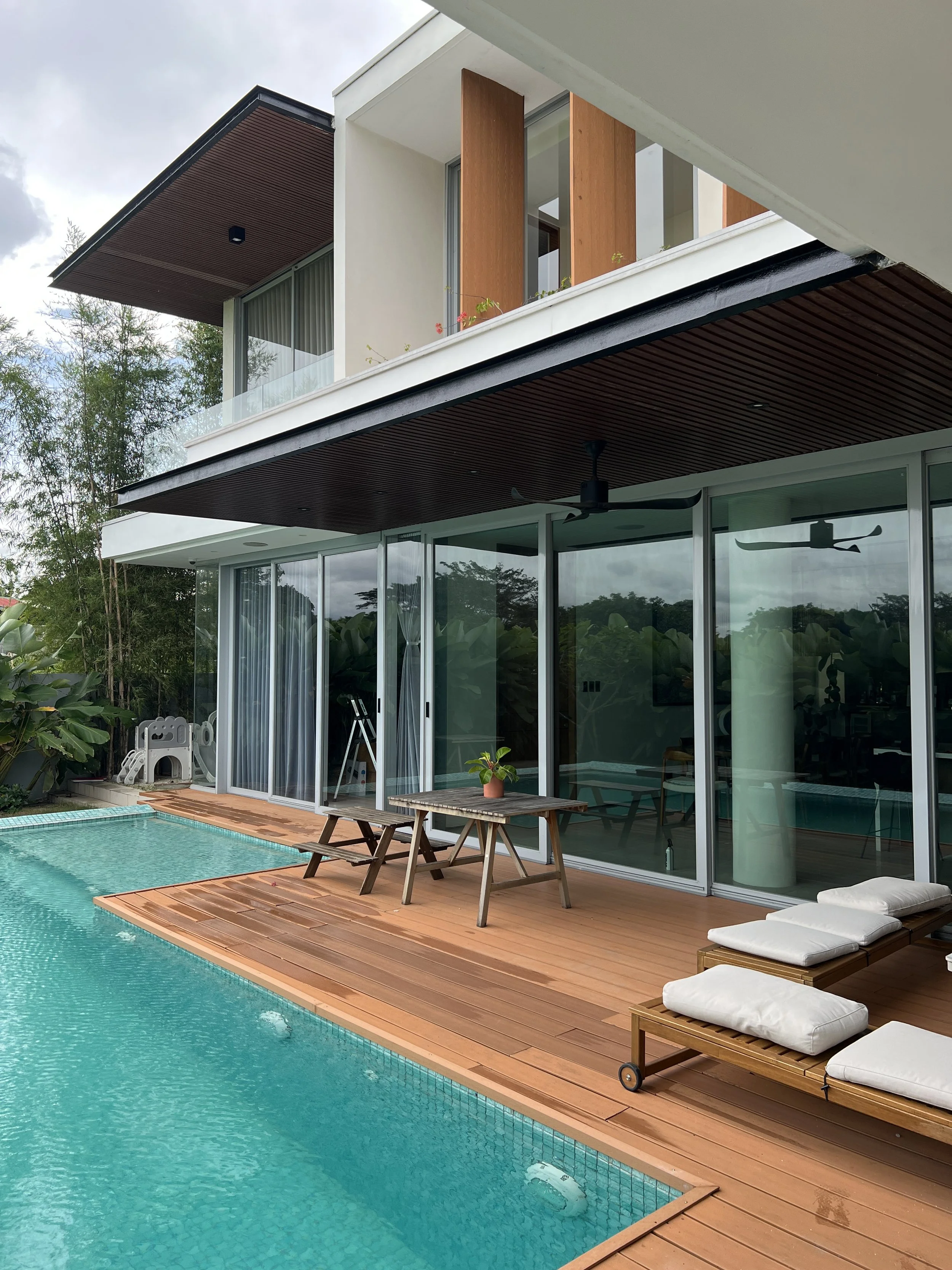 Modern two-story home with large tinted glass sliding doors overlooking a pool and wooden deck, showcasing residential window tint installation
