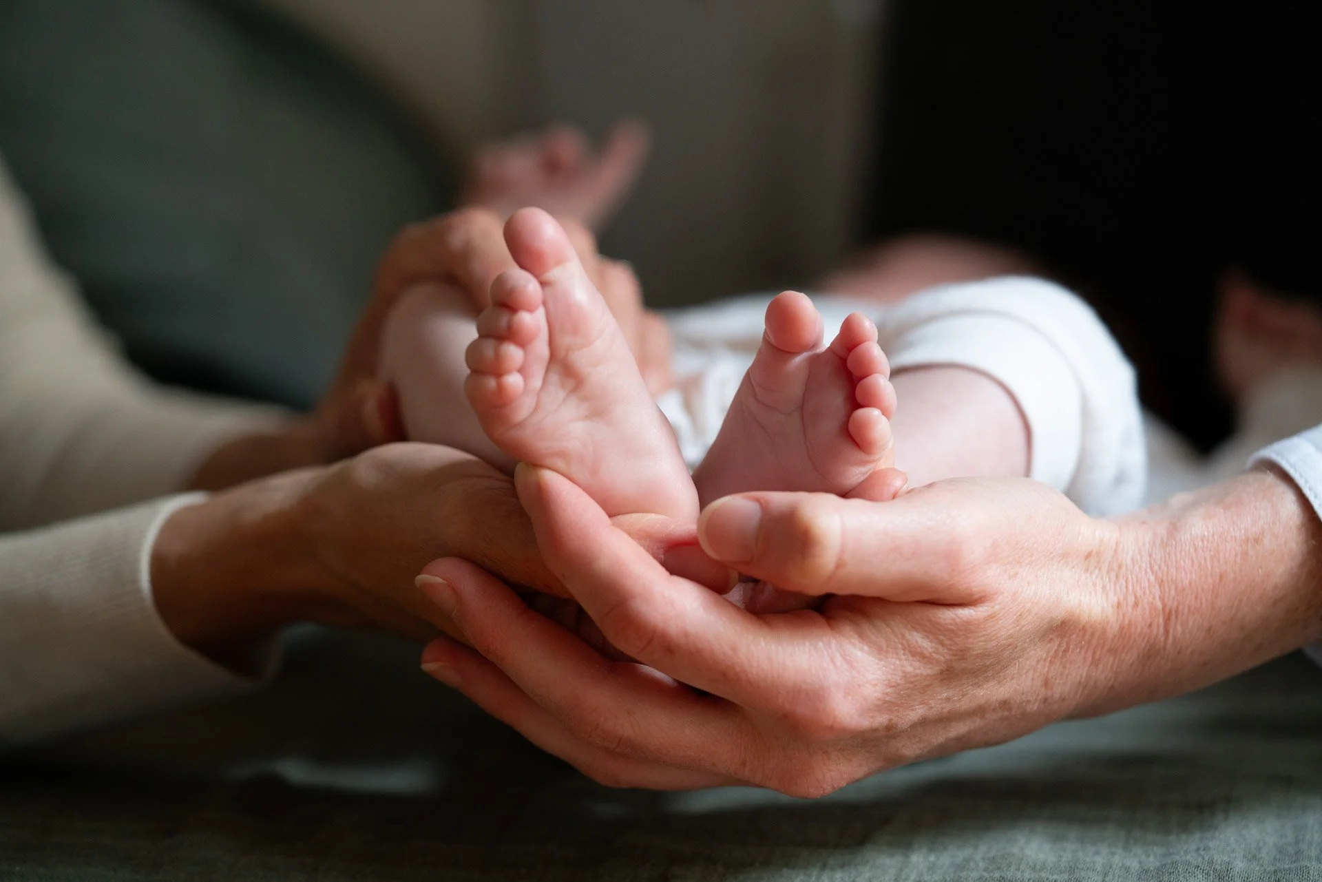 Close-up of a baby's feet being gently held by two adults' hands.