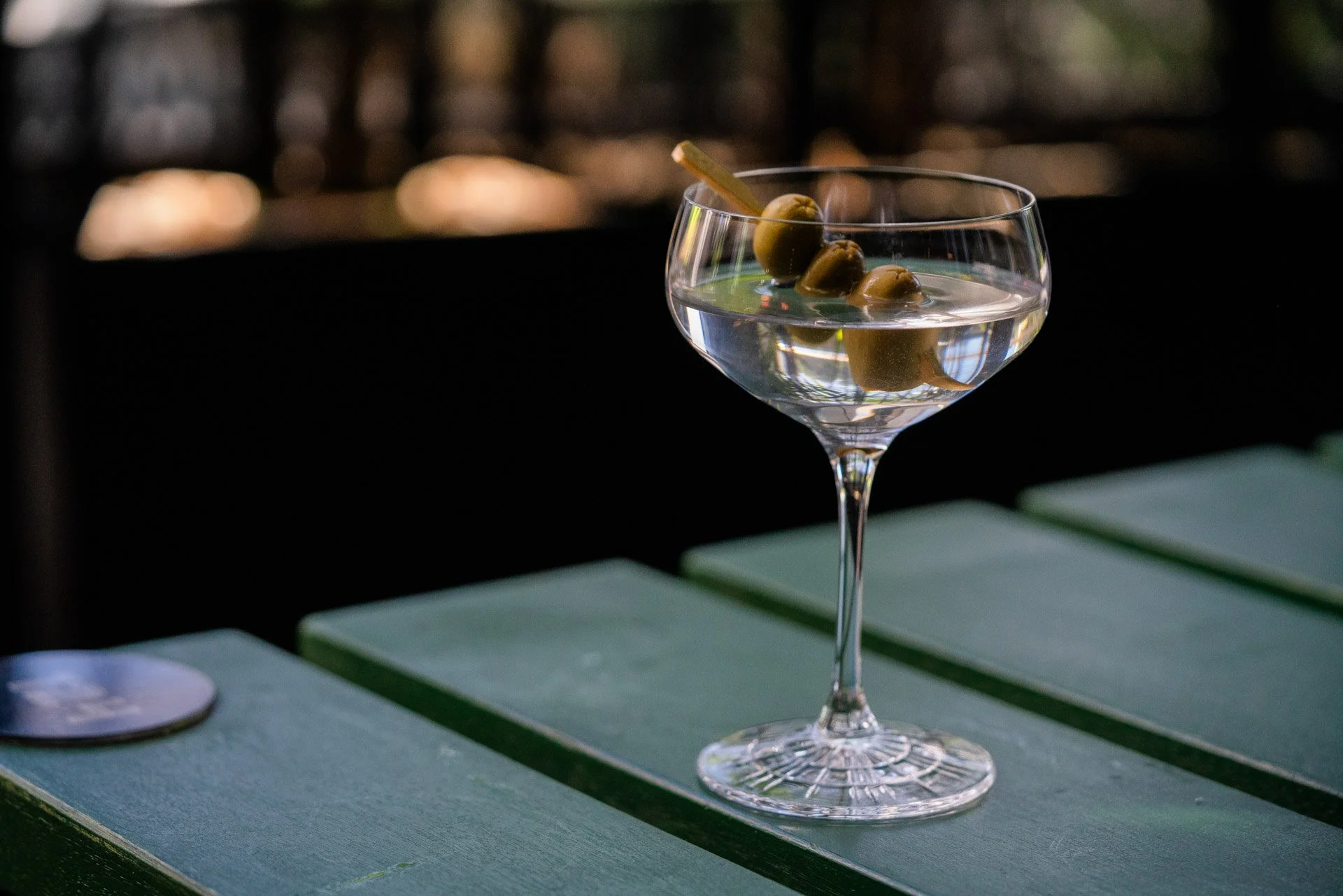 A cocktail glass filled with a clear drink garnished with green olives on a skewers