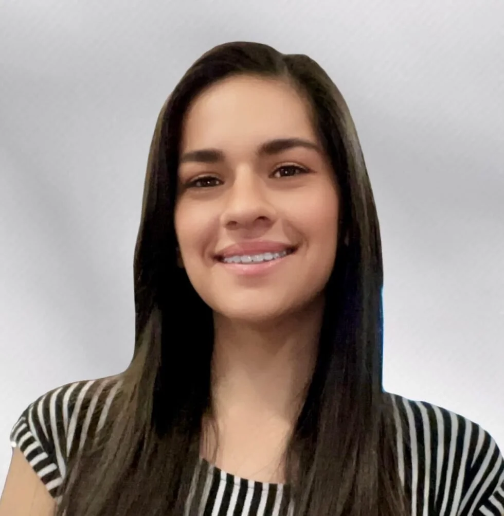A young woman with long dark hair smiling at the camera, wearing a black and white striped top, against a plain light-colored background.