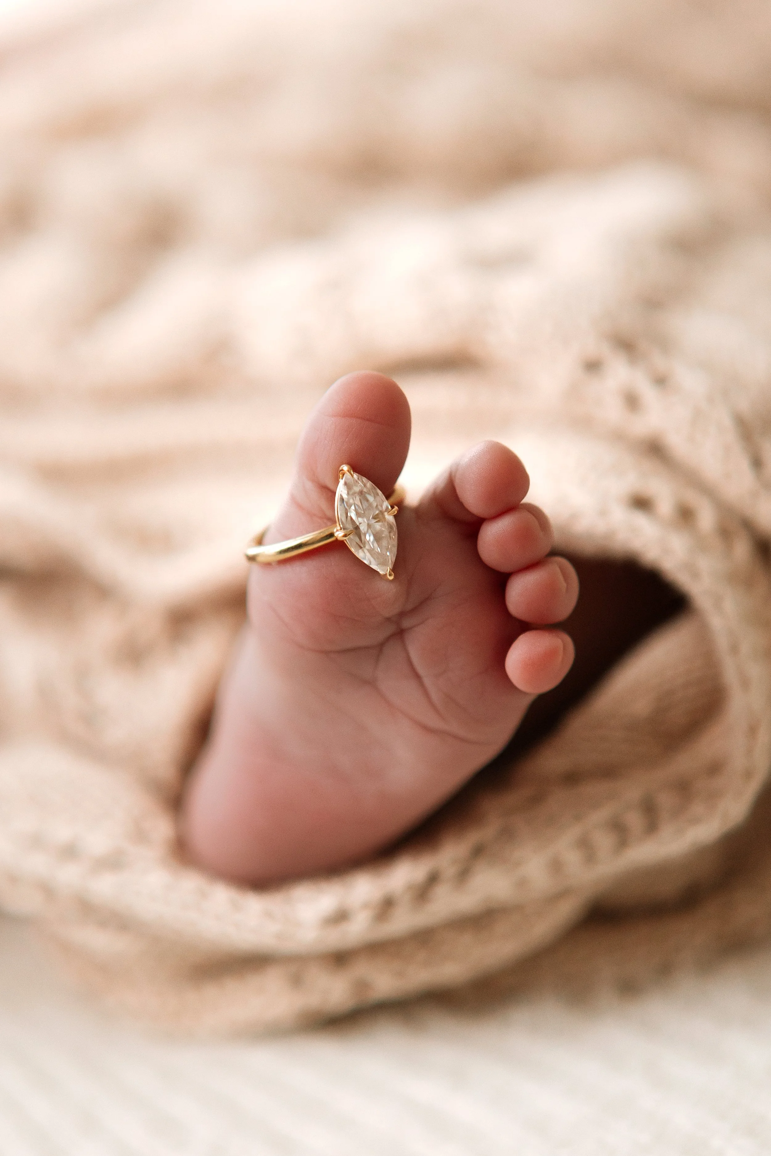 Close-up of a hand with a large, clear gemstone ring on the middle finger, resting on a soft, beige, textured fabric background.