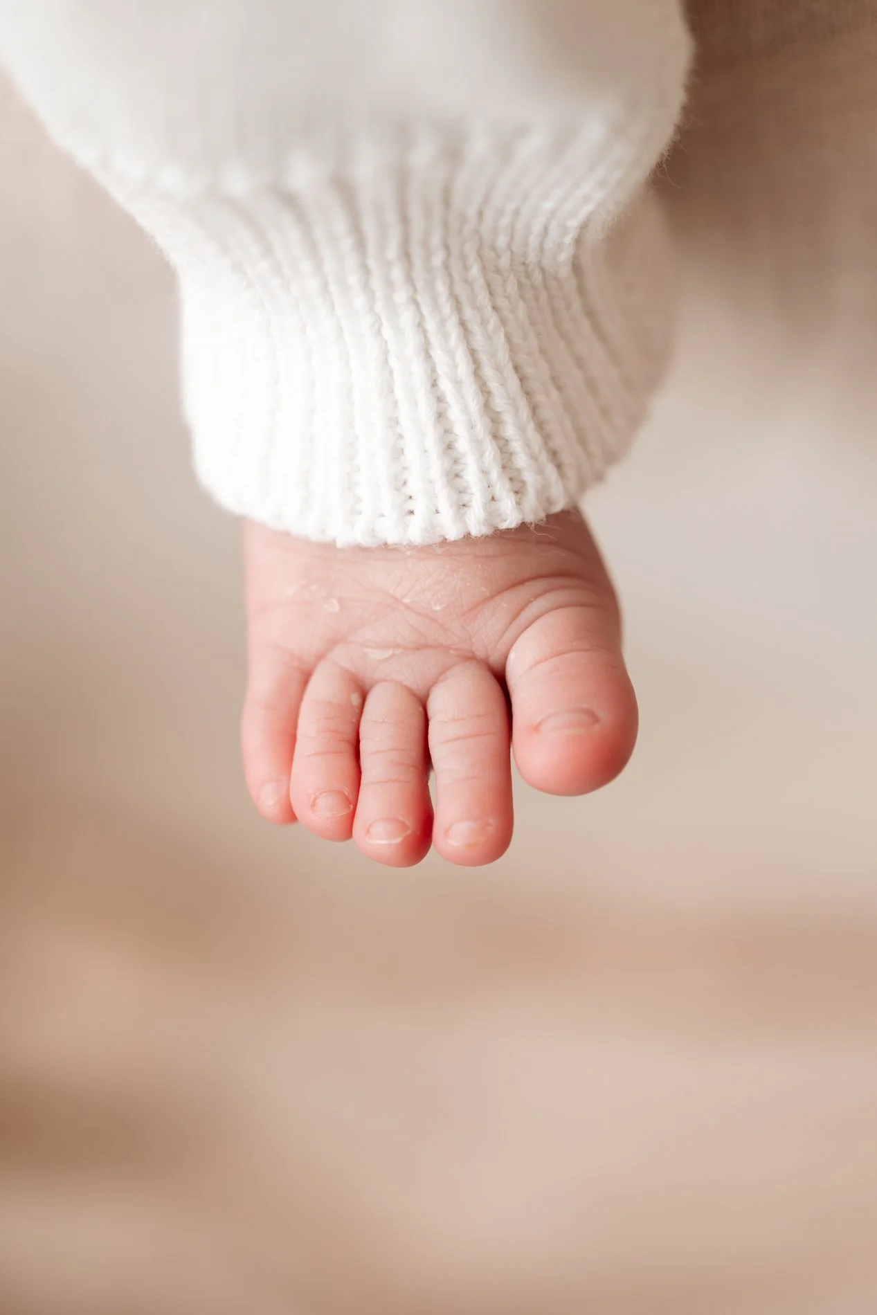 Close-up of a baby's foot in a cream-colored knit sweater.