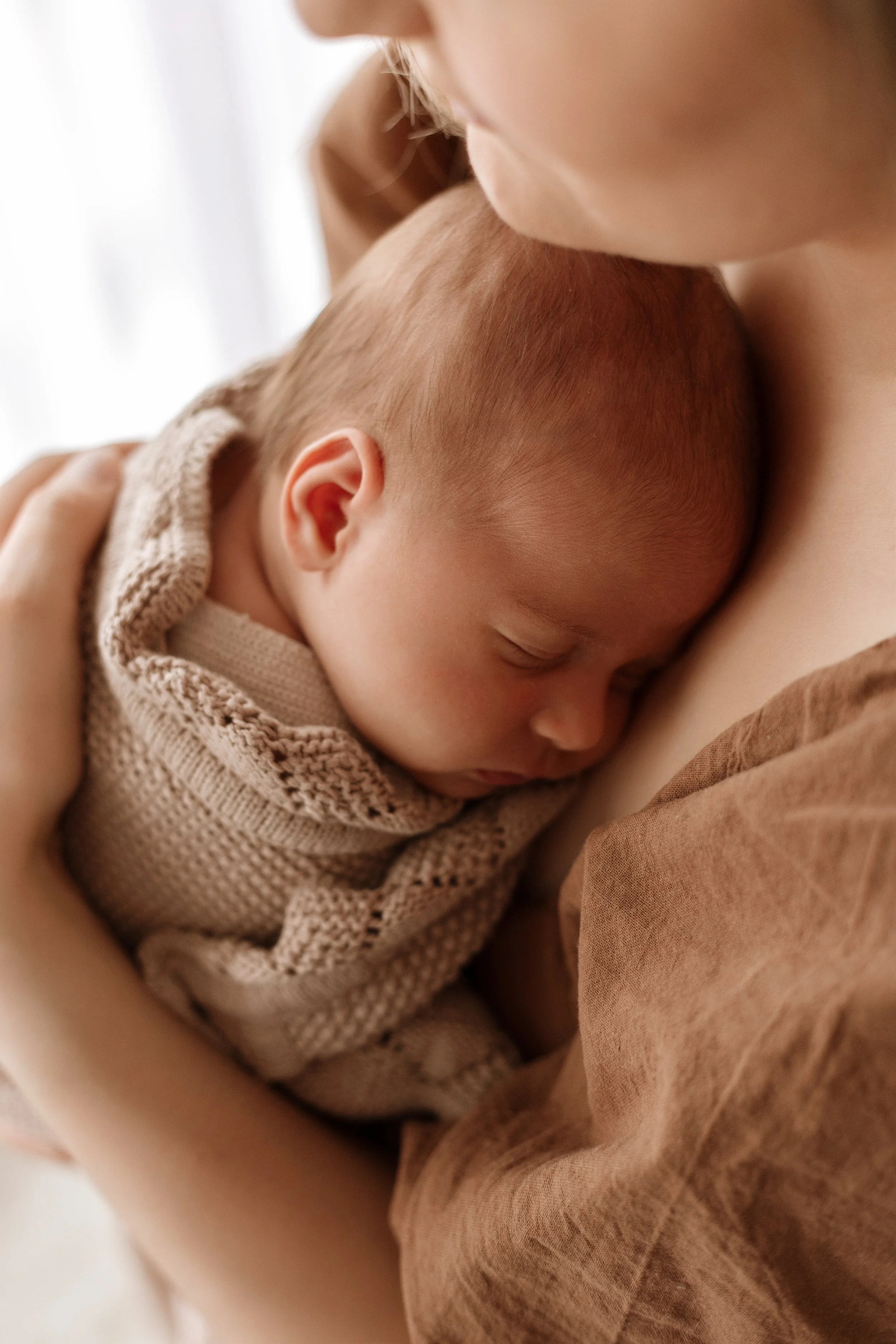 A tender moment of a mother holding her sleeping newborn baby close against her chest in a cozy setting.