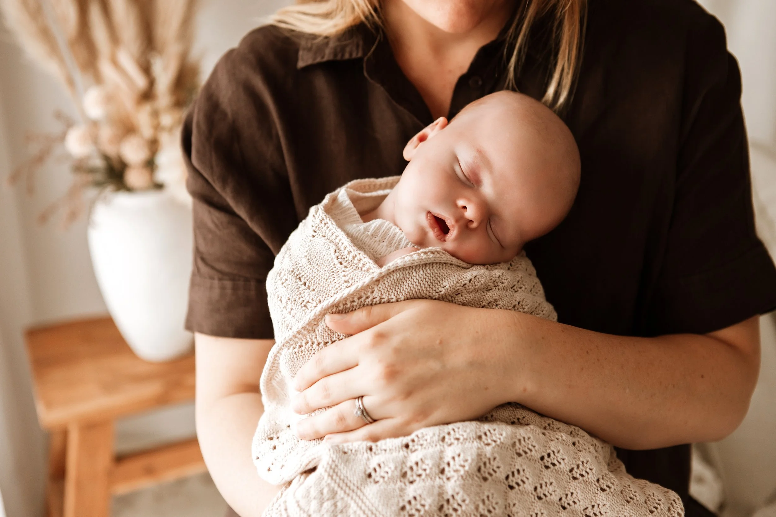 A woman holding a sleeping baby wrapped in a knitted blanket.