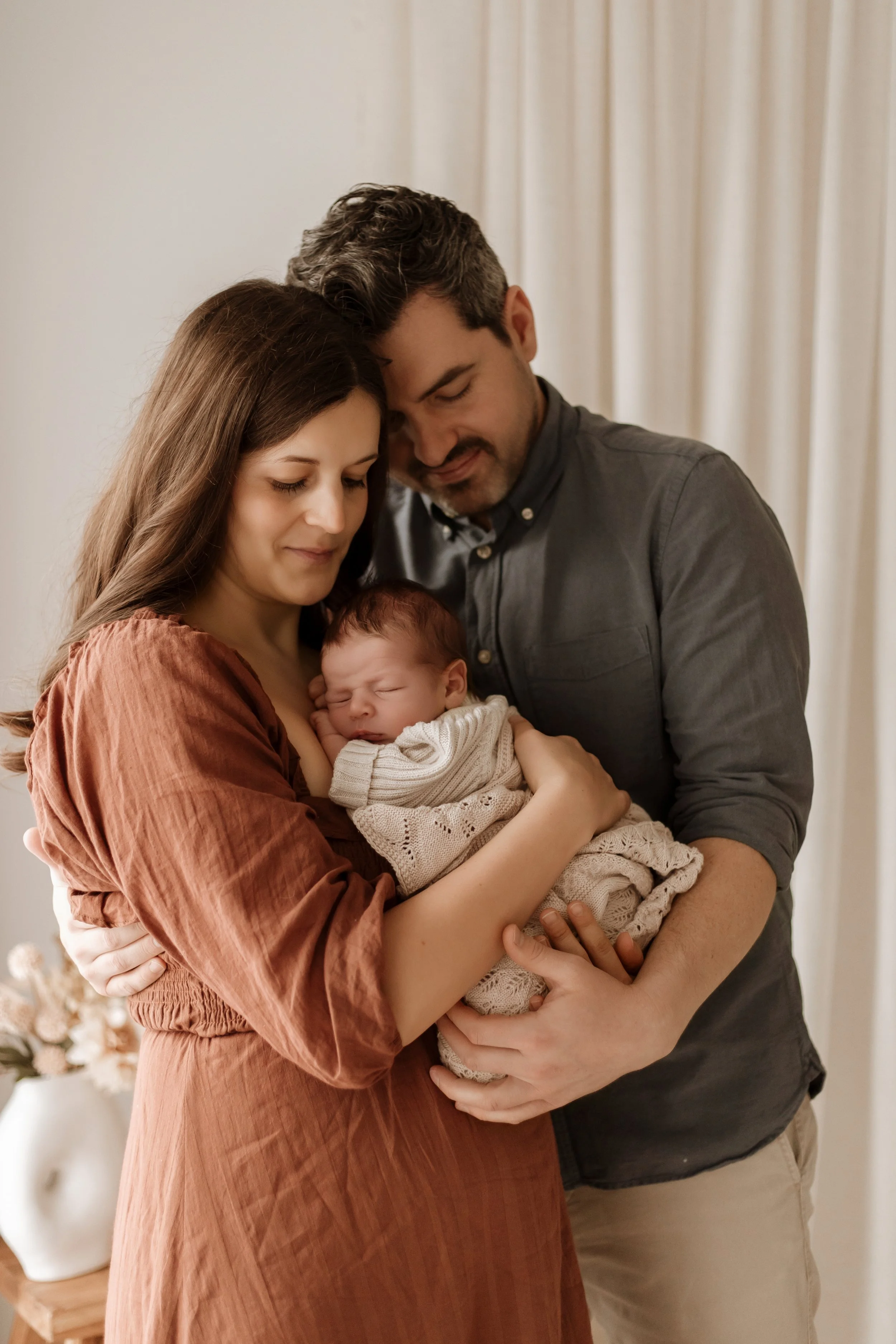 A mother, father, and newborn baby sharing a tender moment indoors.