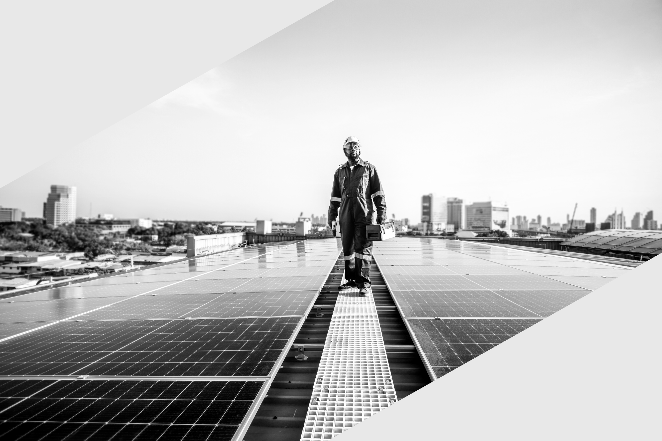 Ein Techniker in Arbeitskleidung und Helm läuft auf einer Dachfläche mit Solarzellen, hält eine Werkzeugkiste und einen Werkzeugkasten, im Hintergrund eine Stadt mit Hochhäusern.