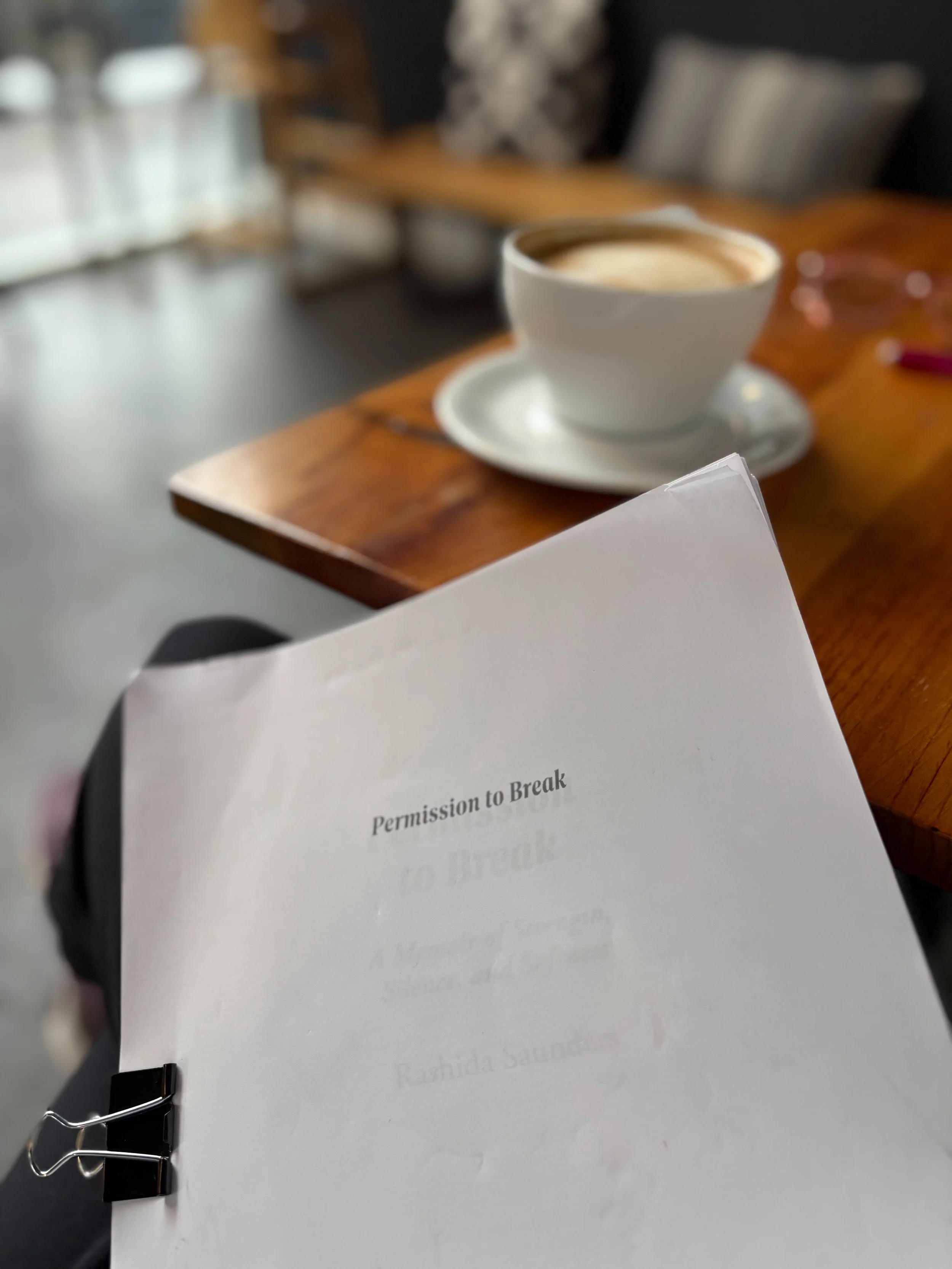 Printed manuscript pages titled “Permission to Break” resting on a table beside a cup of coffee.