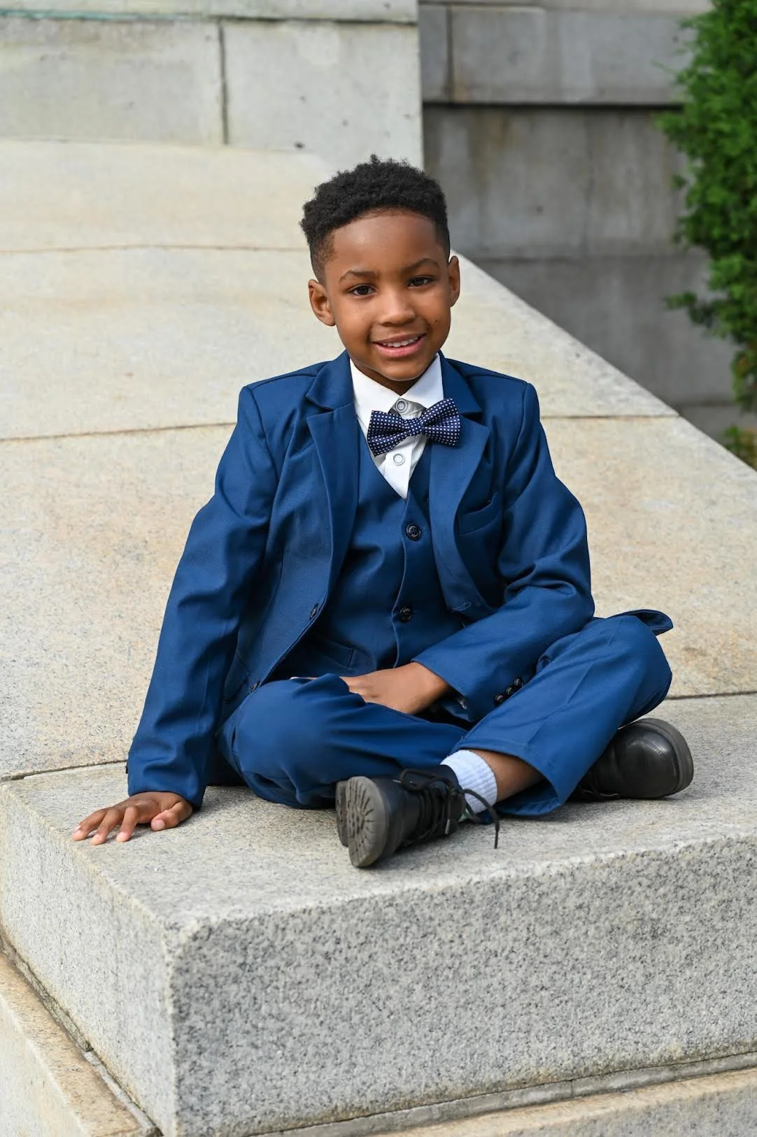 Young child dressed in a blue suit sitting on stone steps during a portrait session.