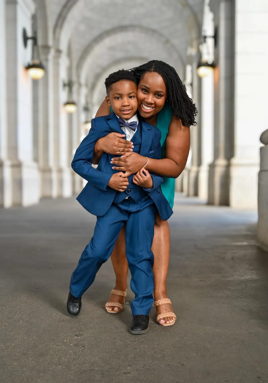 Woman embracing a young child during an outdoor portrait session beneath an archway.