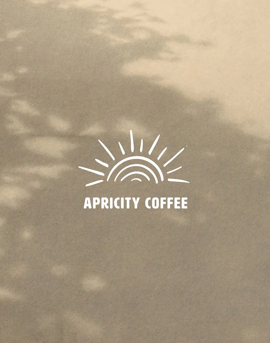 A cloudy sky with a neon-like sun rising and the text 'APRICITY COFFEE' below it.
