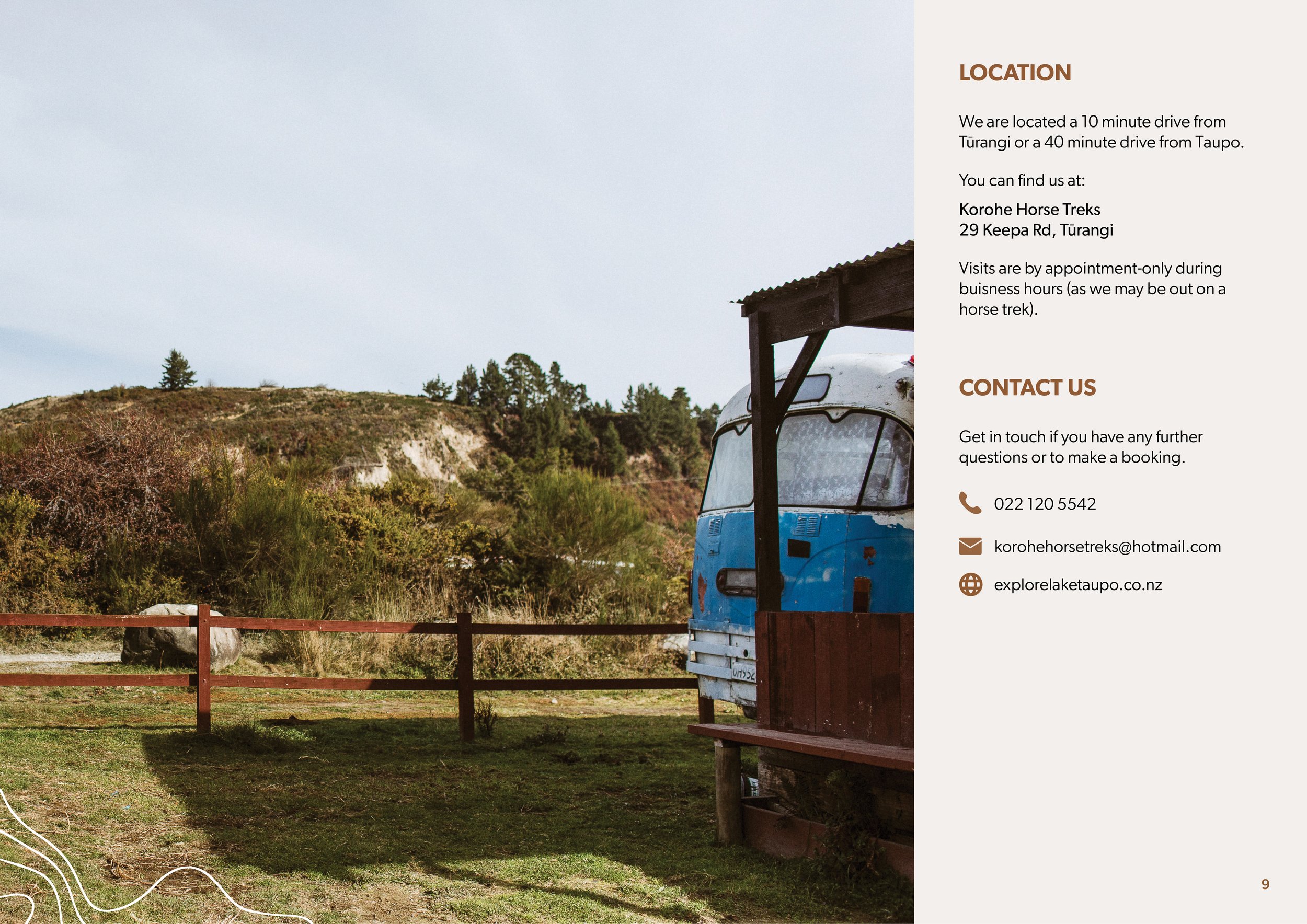 A scenic outdoor view with green grassy ground, a wooden fence, and a hilly landscape with trees in the background. On the right side, part of a blue and white vintage vehicle or trailer is visible under a small wooden structure.