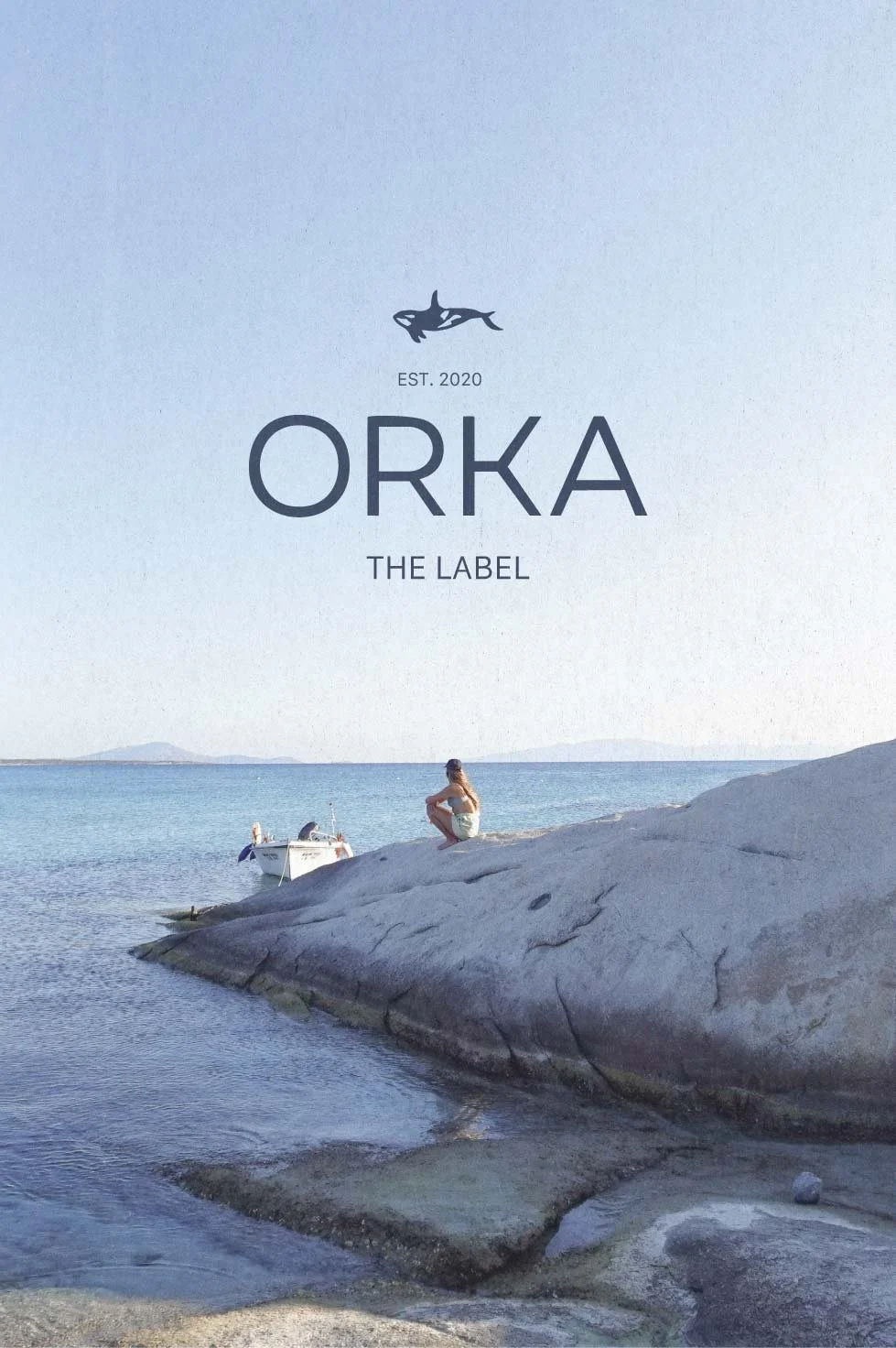 A woman sits on a large rock by the water, with a small boat anchored nearby on a calm sea, under a clear sky with distant landmasses on the horizon, on the cover of Orka's label featuring a fish logo and the text 'EST. 2020' and 'THE LABEL'.