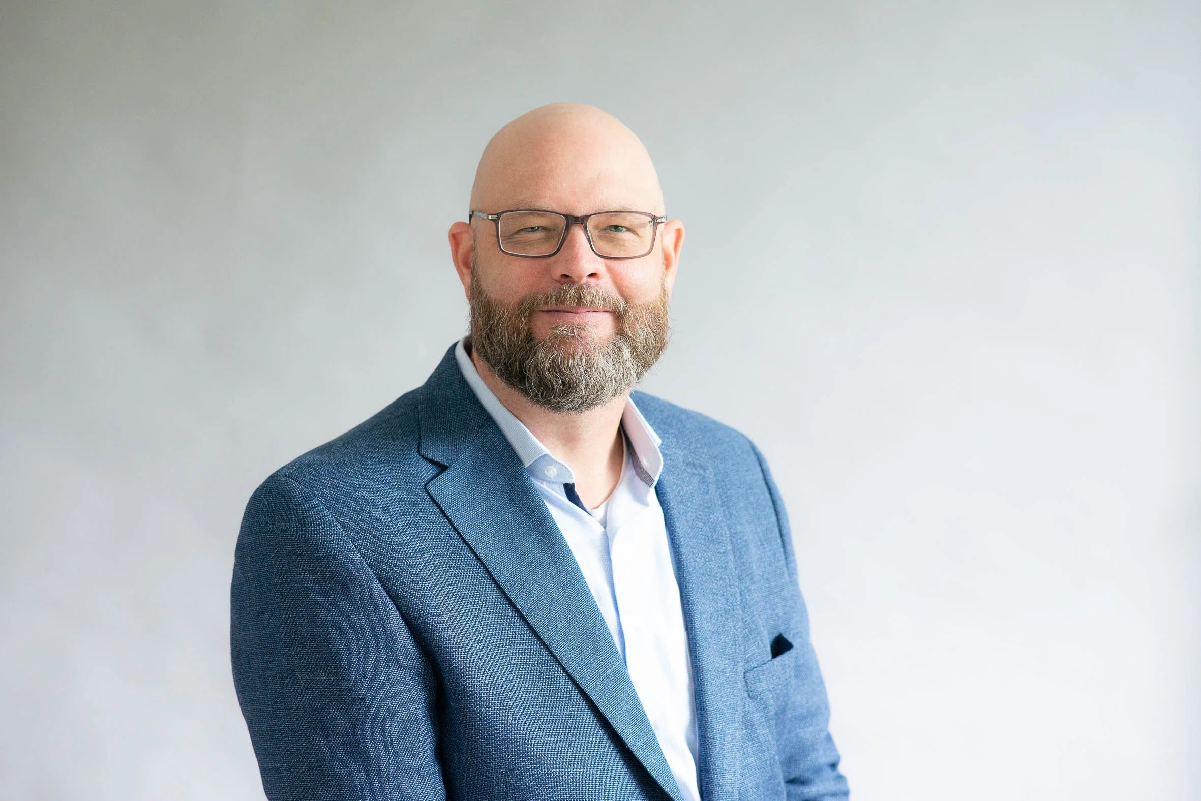 Porträt eines Mannes in einem blauen Anzug und Brille vor hellem Hintergrund.