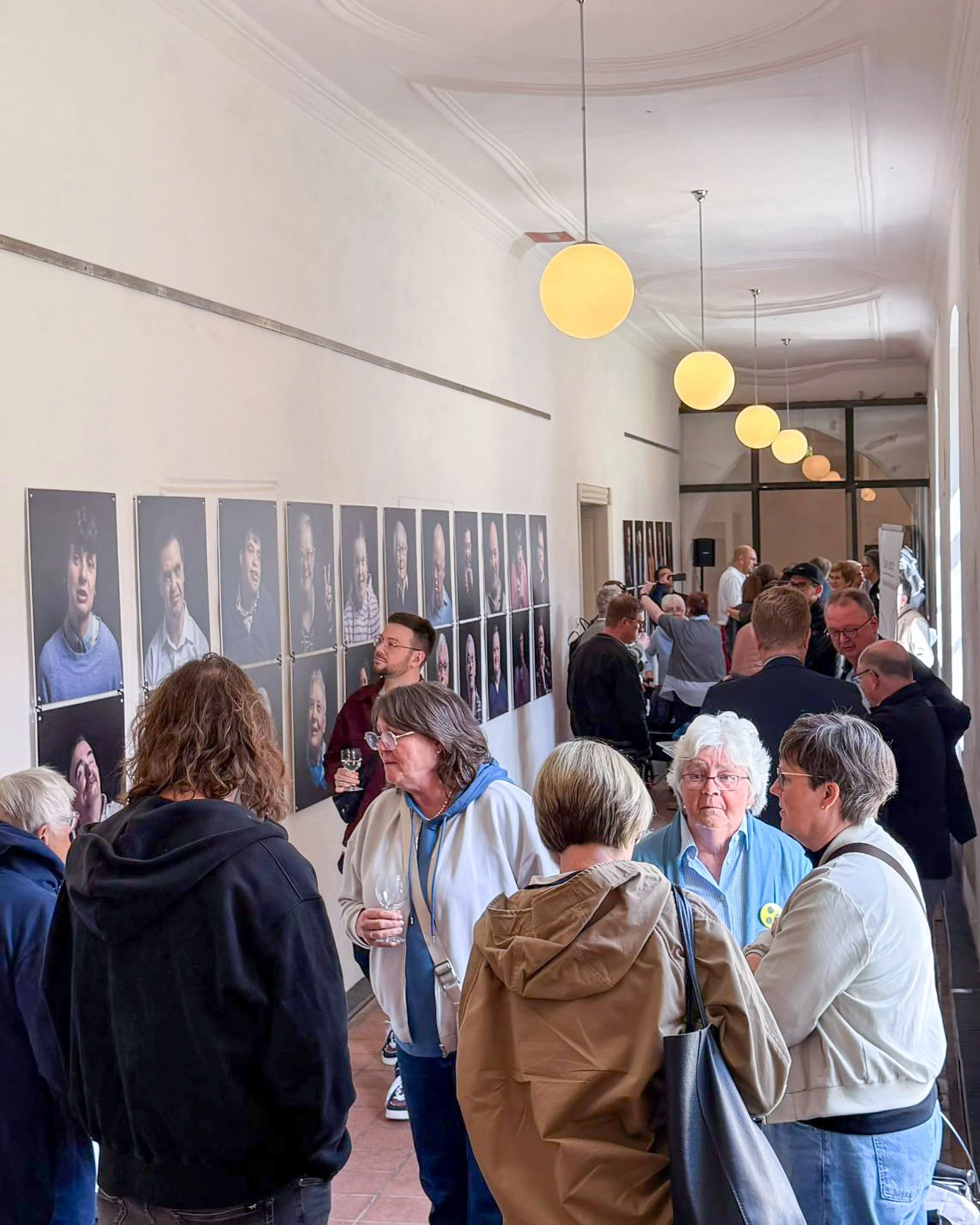 Menschen versammelt in einem Raum mit Porträts an der Wand, die Ausstellung Starke Gesichter wird eröffnet