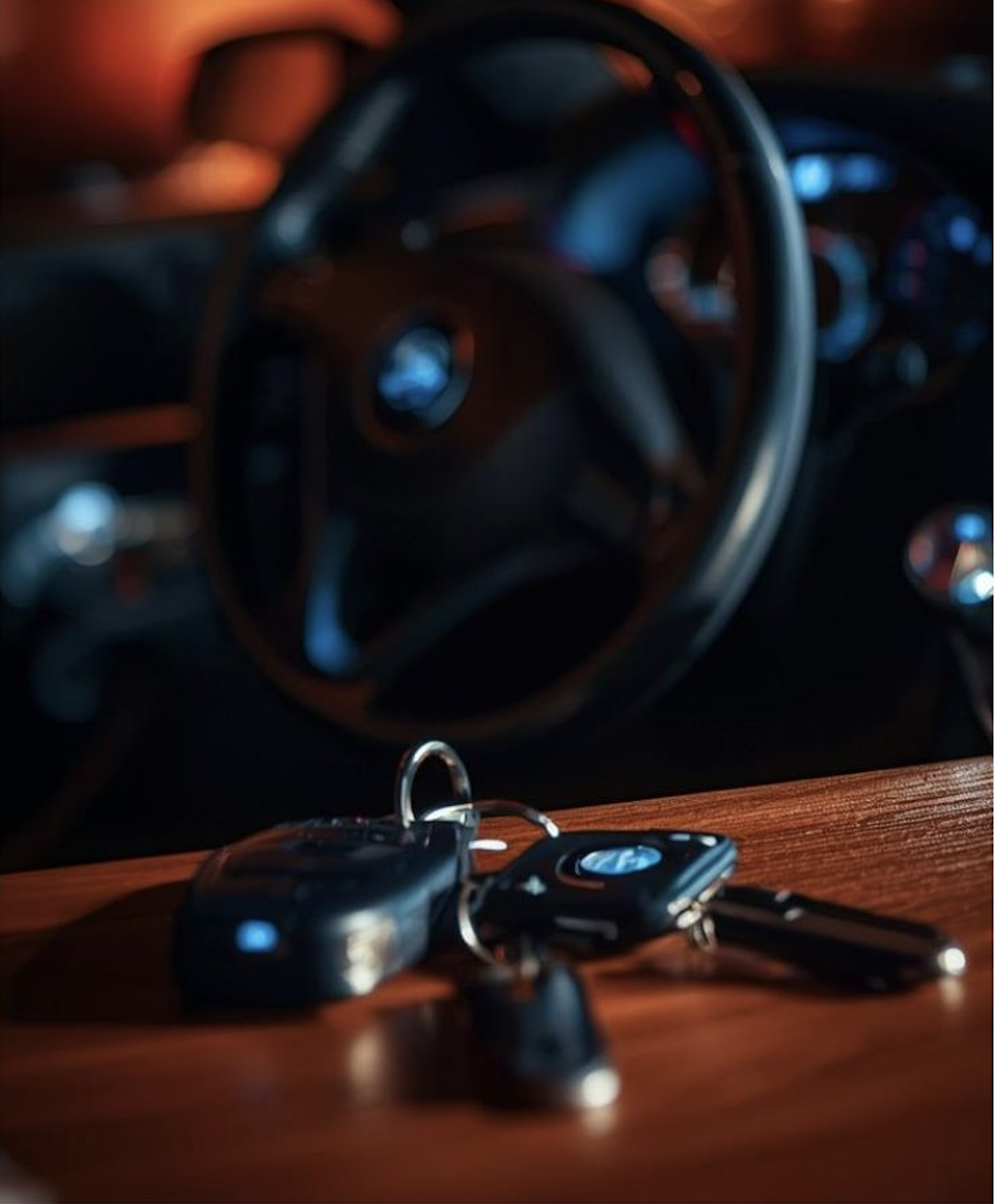 Claus de cotxe recolzades sobre una superfície de fusta davant d'un tauler de control i un volant borrosos en un entorn poc il·luminat.